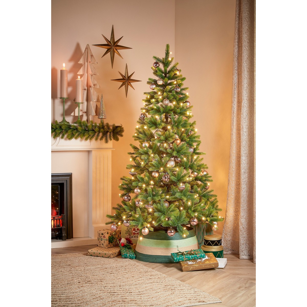 A decorated Christmas tree with lights and baubles stands in a room with a fireplace.