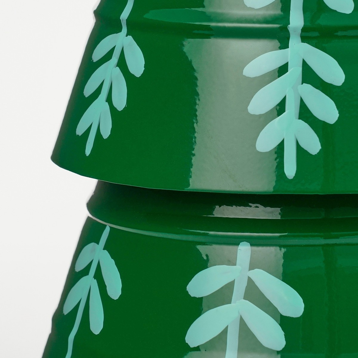 Two glossy green bowls stacked, decorated with light blue leaf patterns against a plain white background.