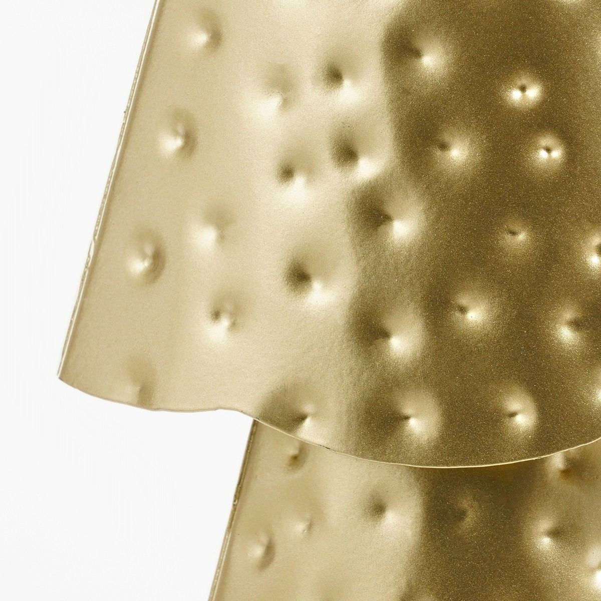 Close-up of a textured, hammered gold metal surface with a pattern of dimples against a plain white background.