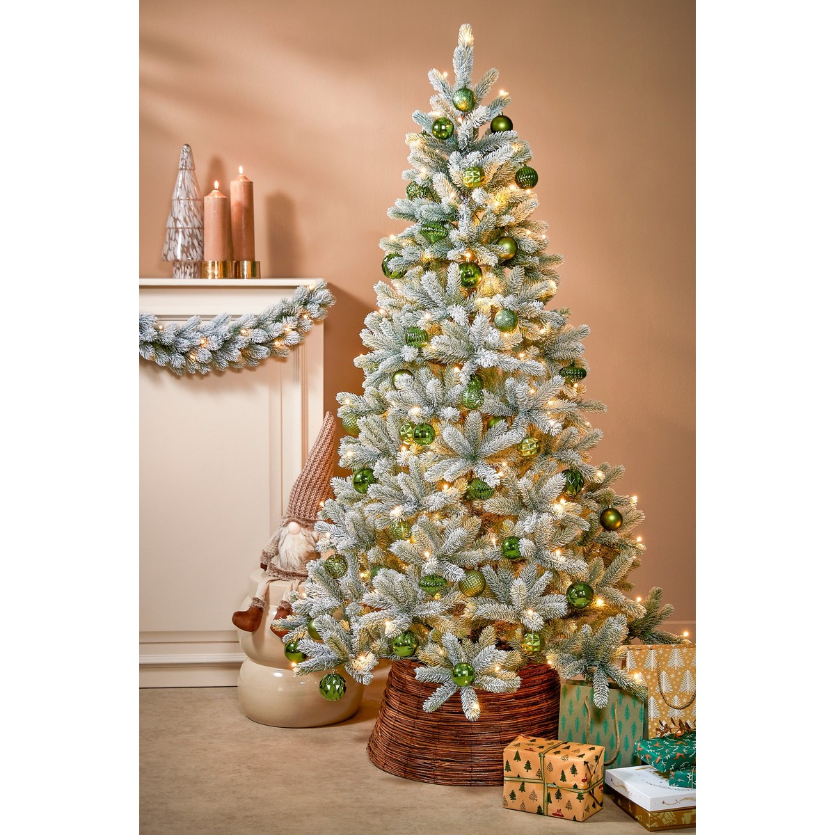 A snowy Christmas tree decorated with green baubles and lights, with gifts underneath.