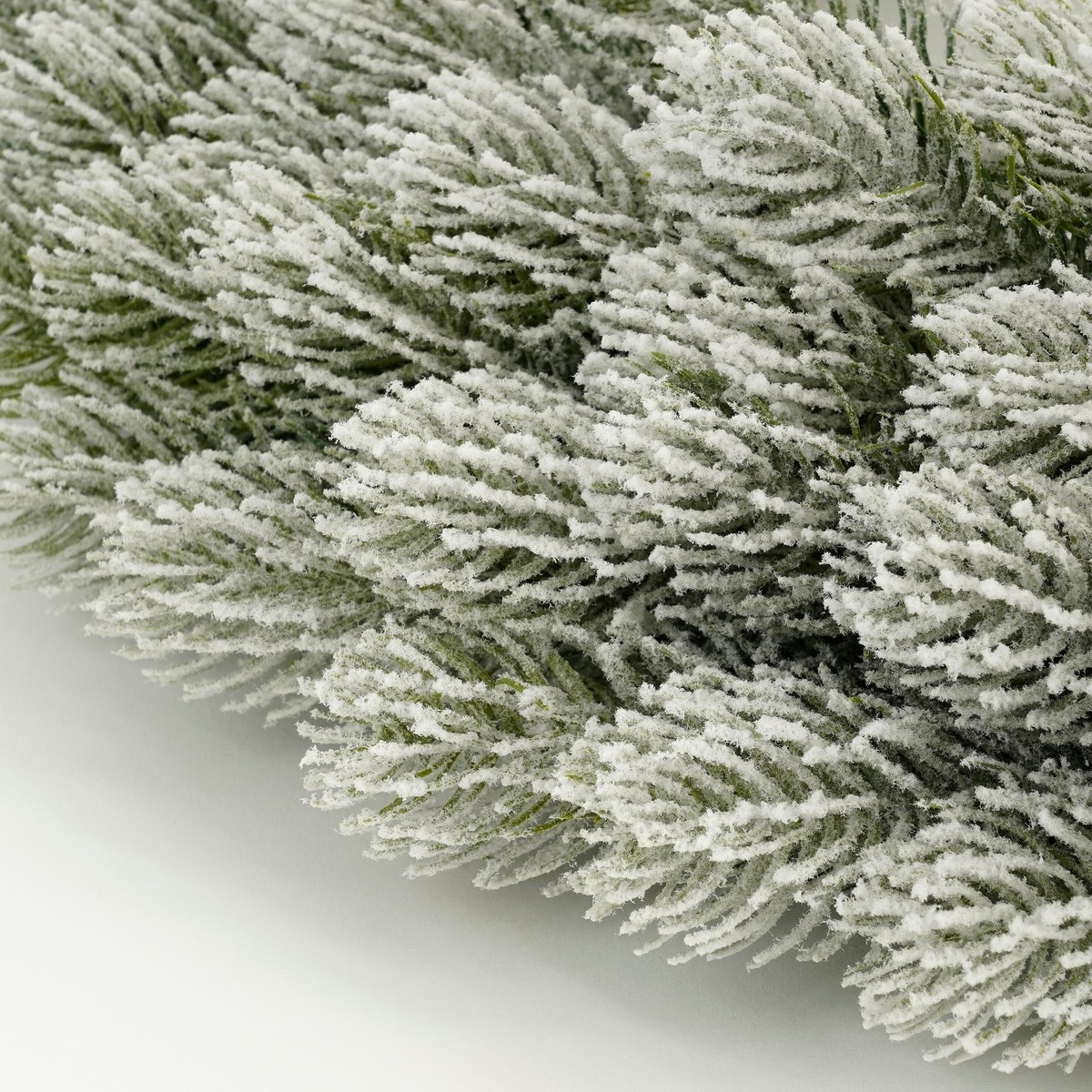 Close-up of an artificial pine branch with dense white snow covering its needles.