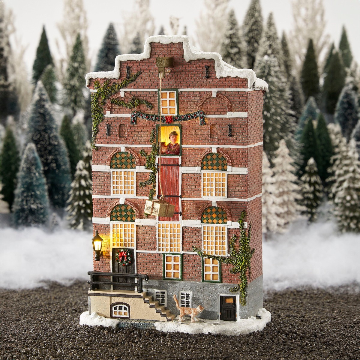 Illuminated Christmas brick house in a snowy forest landscape with crane and figurine.