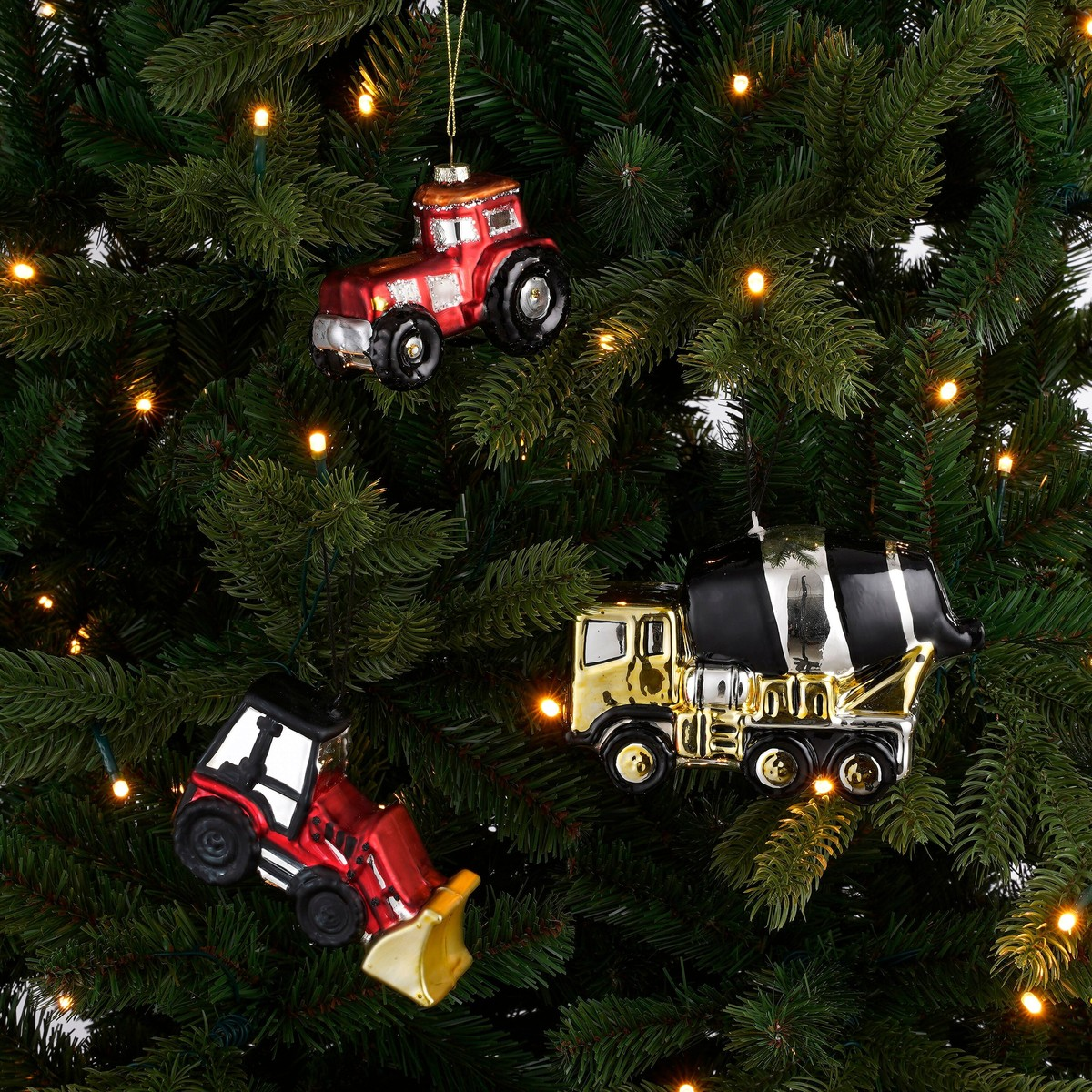 Three vehicle-themed Christmas ornaments hang on a decorated pine tree.