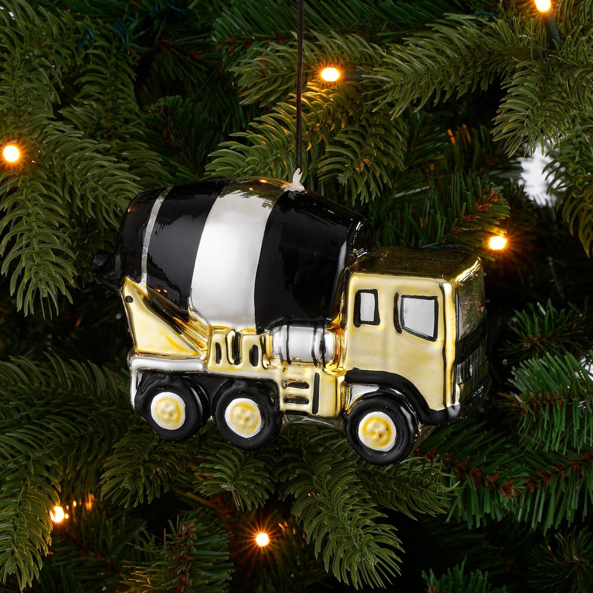 A shiny gold cement mixer truck Christmas ornament hanging in green pine branches.