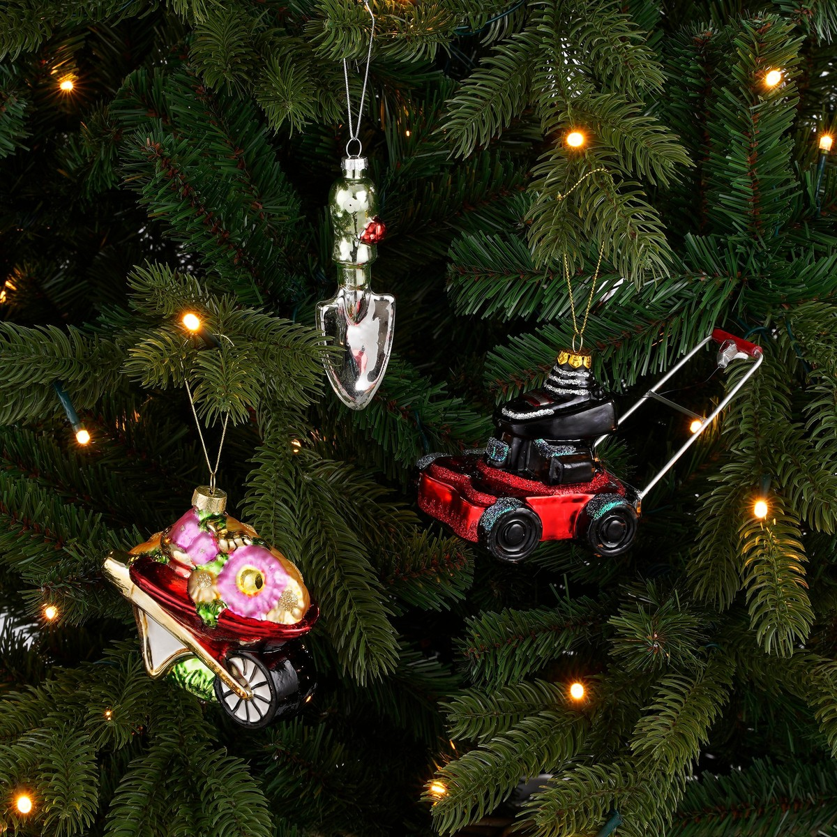 Gardening tools as Christmas ornaments hang in a green Christmas tree with lights.