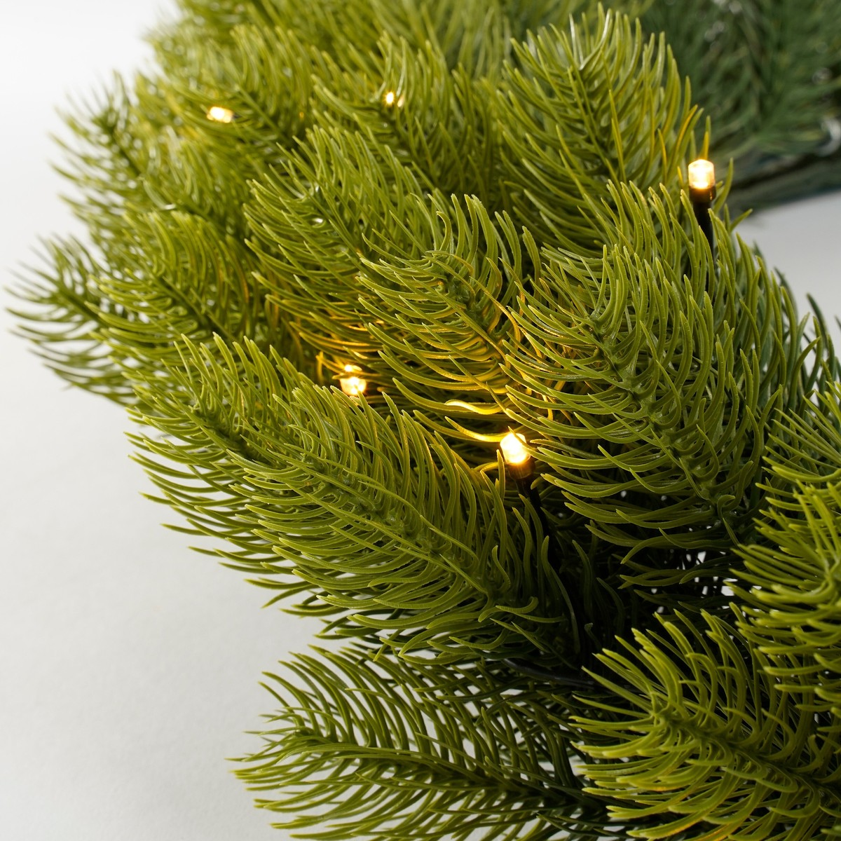 Green artificial pine branches intertwined with small, warm glowing fairy lights.