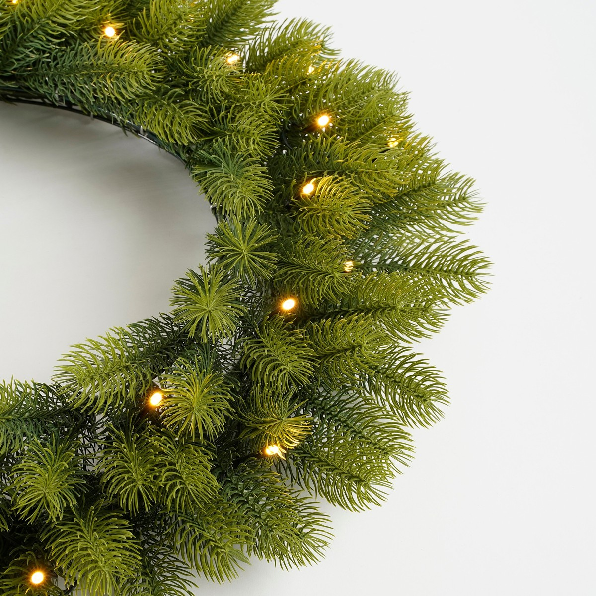 Green pine wreath with warm string lights against a white background.