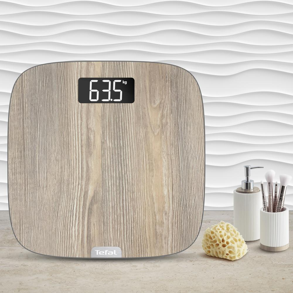 Bilancia Tefal in legno mostra 63.5 kg su marmo con spugna, dispenser e pennelli.