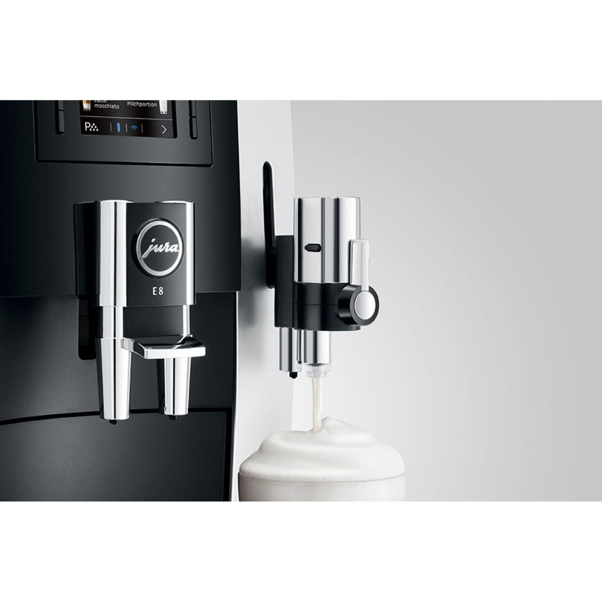 Moderne Jura E8 Kaffeemaschine beim Aufschäumen von Milch in einen Glasbecher vor hellem Hintergrund.