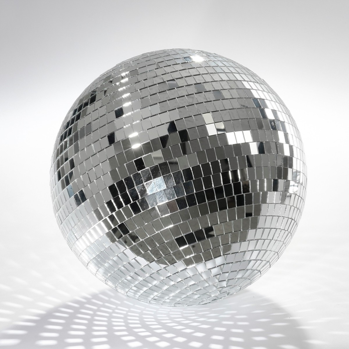 Une boule à facettes argentée brillante sur fond blanc, réfléchissant la lumière et une ombre.