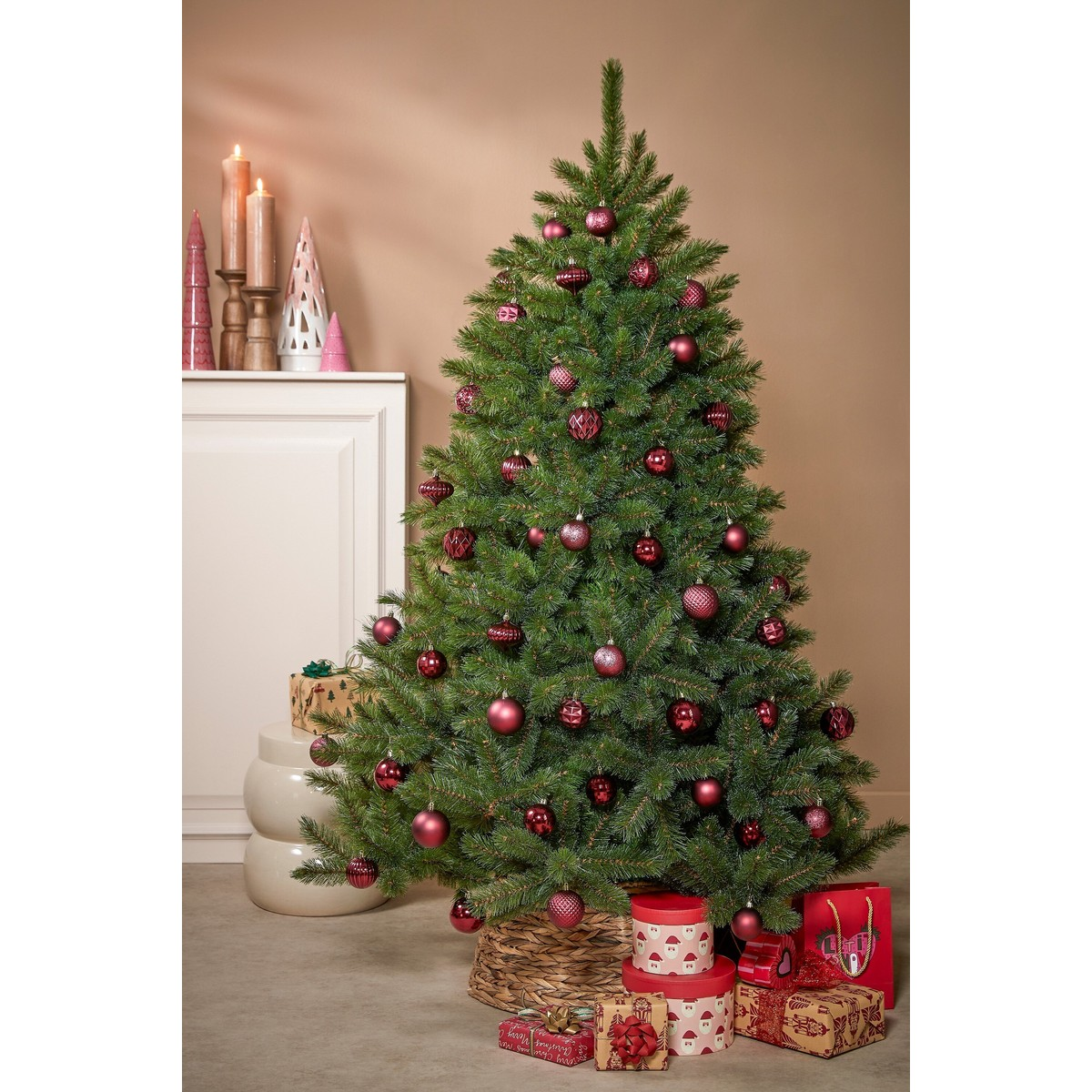 A decorated Christmas tree with red baubles stands in front of a light wall with gifts.