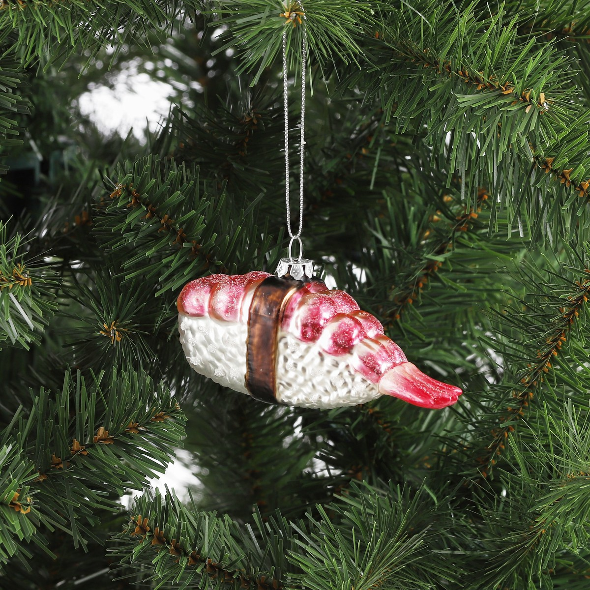 A sushi Christmas ornament shaped like shrimp and rice hangs on an artificial Christmas tree.