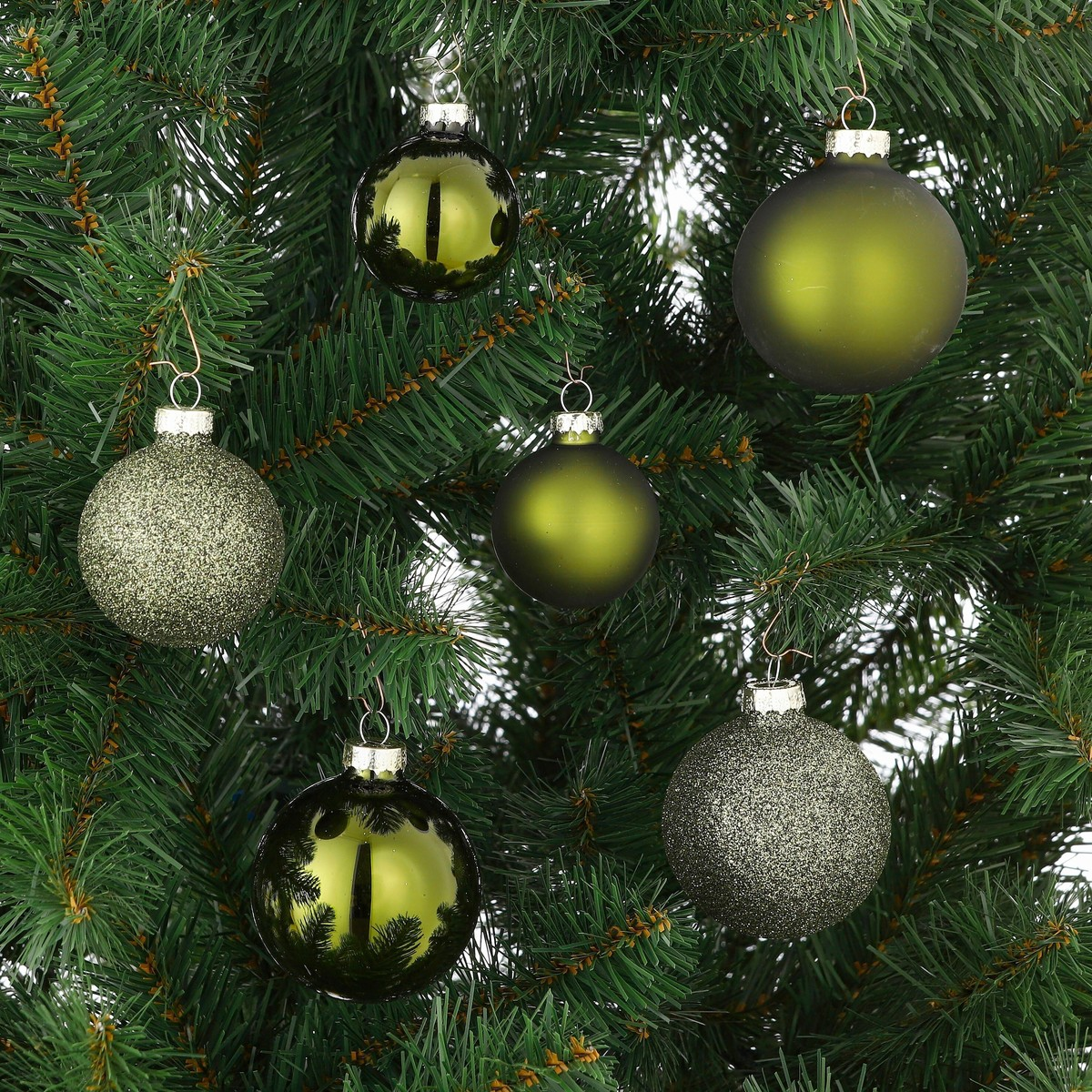 Six green Christmas ornaments hang on the branches of an artificial Christmas tree.