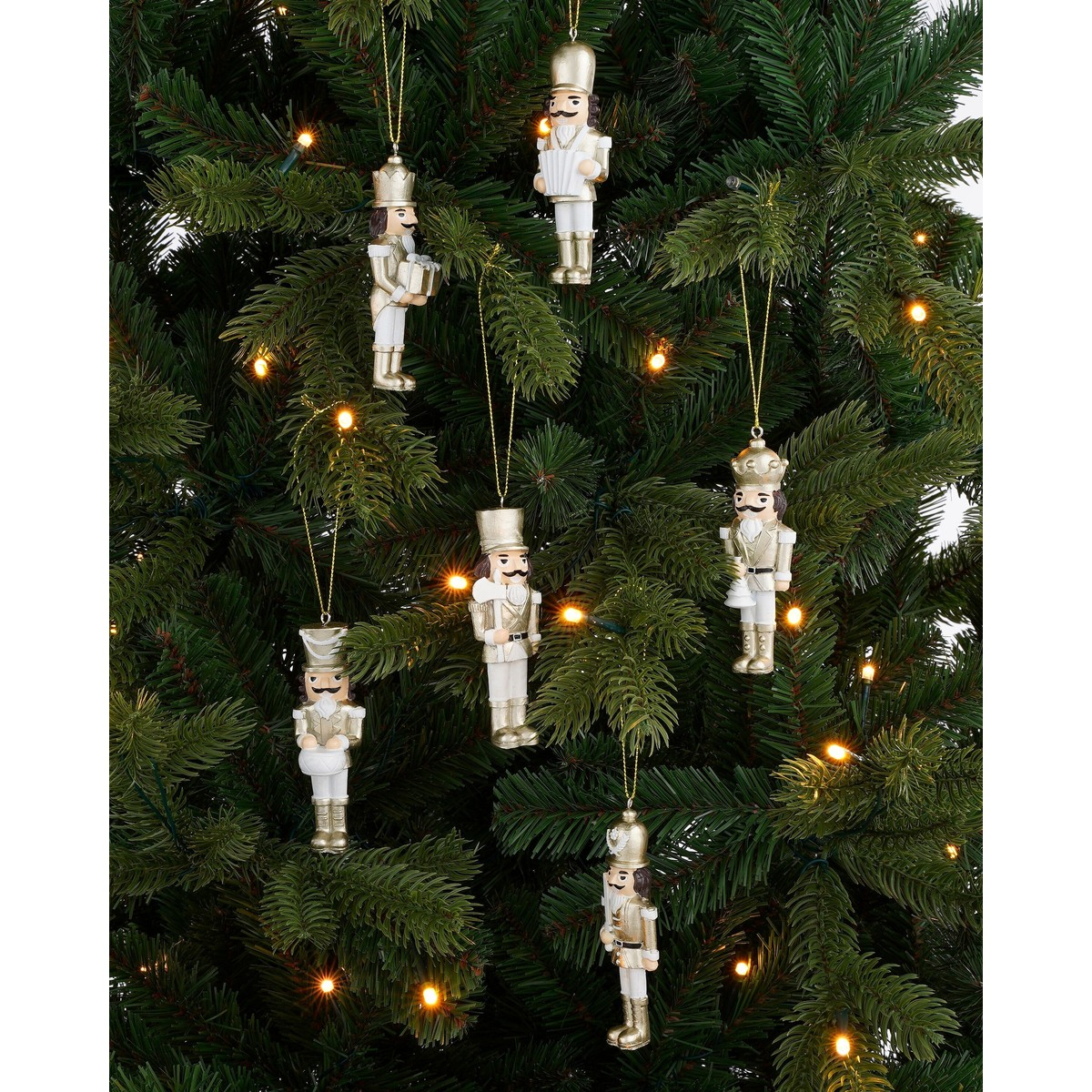Gold and white nutcracker ornaments hang on a green Christmas tree illuminated with warm lights.