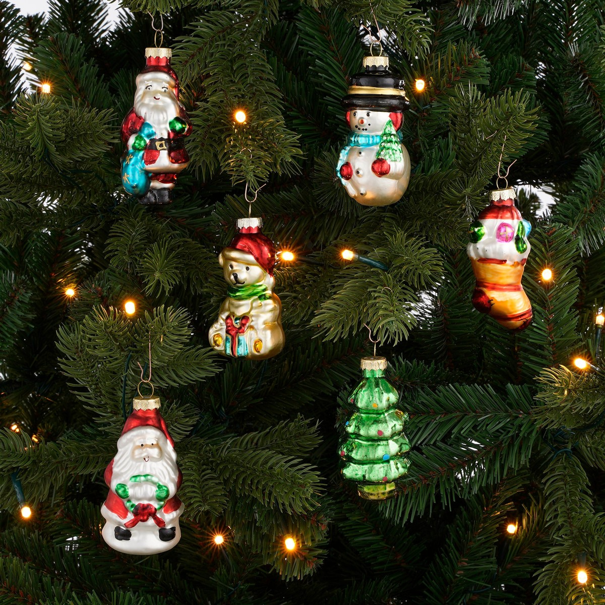Glass Christmas ornaments including Santa, snowman, bear, tree, and stocking hanging on a decorated tree.