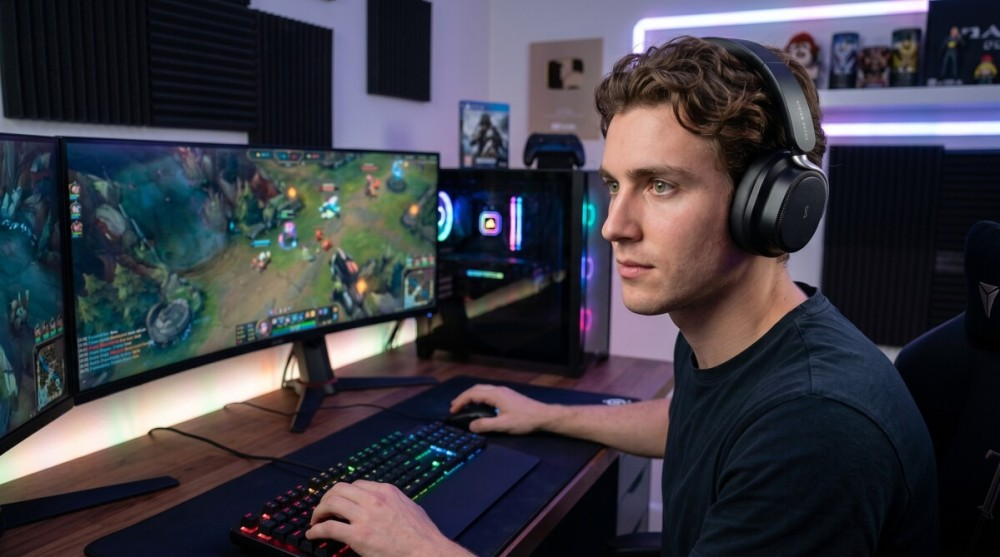 Ein junger Mann mit Kopfhörern spielt in einem Raum mit leuchtenden Lichtern ein Videospiel am Computer.