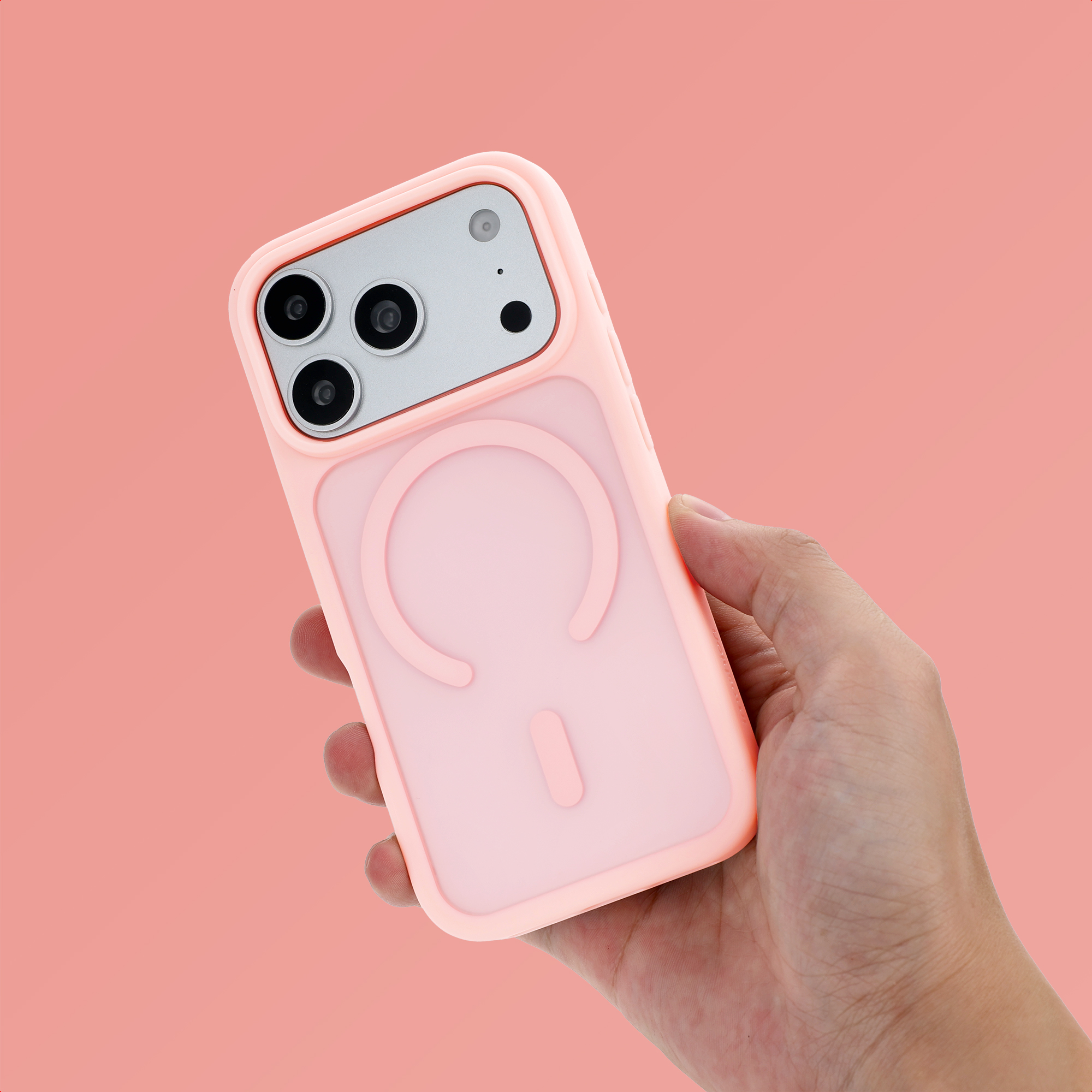 Une main tient un smartphone rose avec une coque de protection sur un fond rose uni.