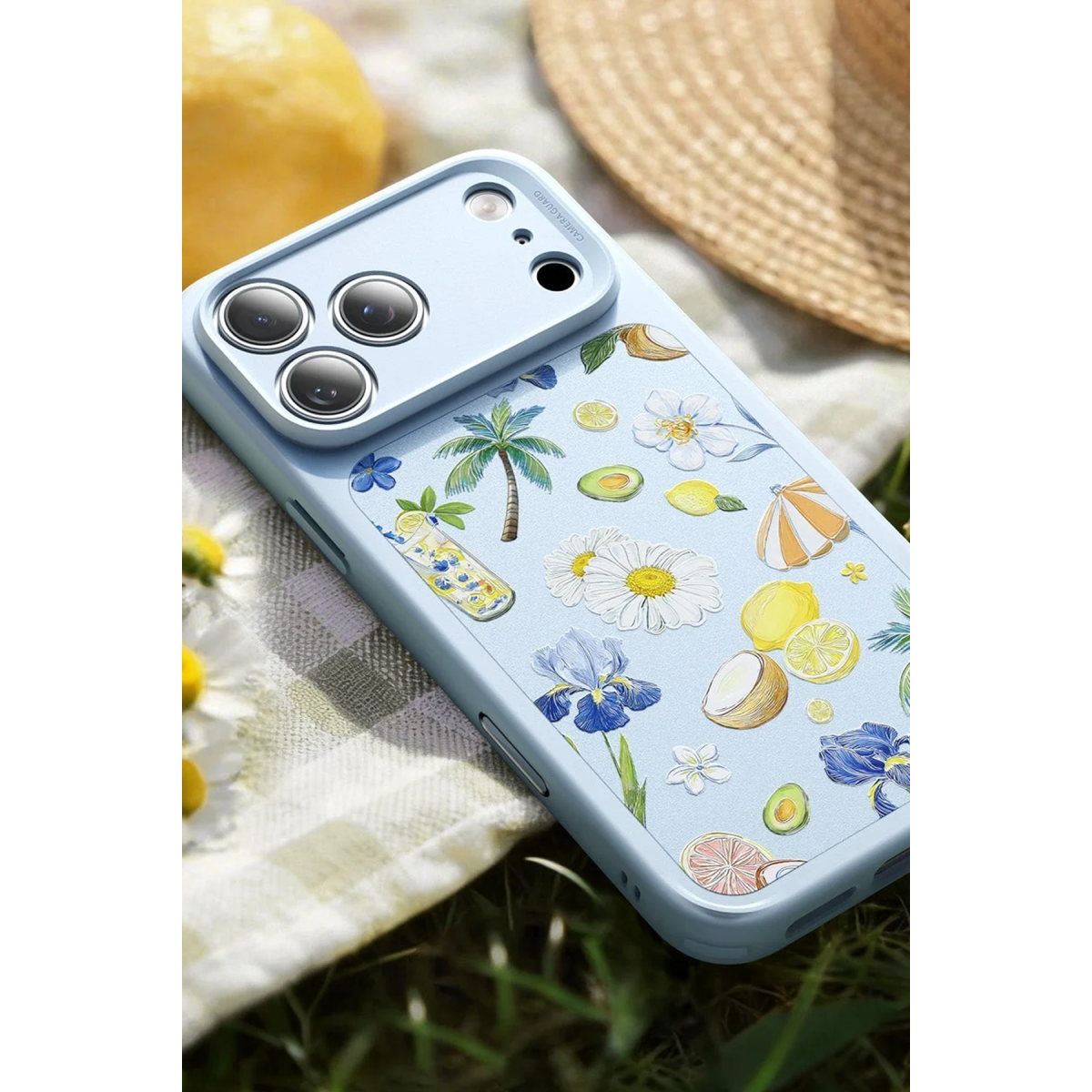 Piknik örtüsü üzerinde palmiye ağaçları, limonlar ve çiçekler gibi tropikal illüstrasyonlara sahip açık mavi telefon kılıfı.