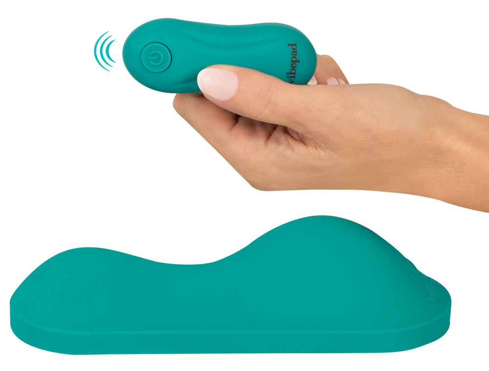 Eine Hand hält eine türkise Fernbedienung über einem wellenförmigen türkisen Kissen.