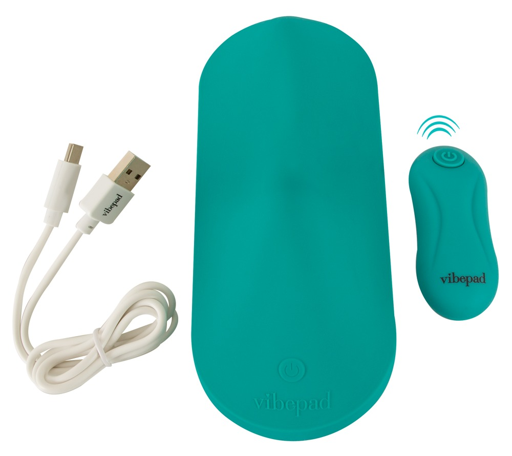 Türkisfarbener Vibepad mit weißem Ladekabel und kleiner Fernbedienung auf weißem Hintergrund.