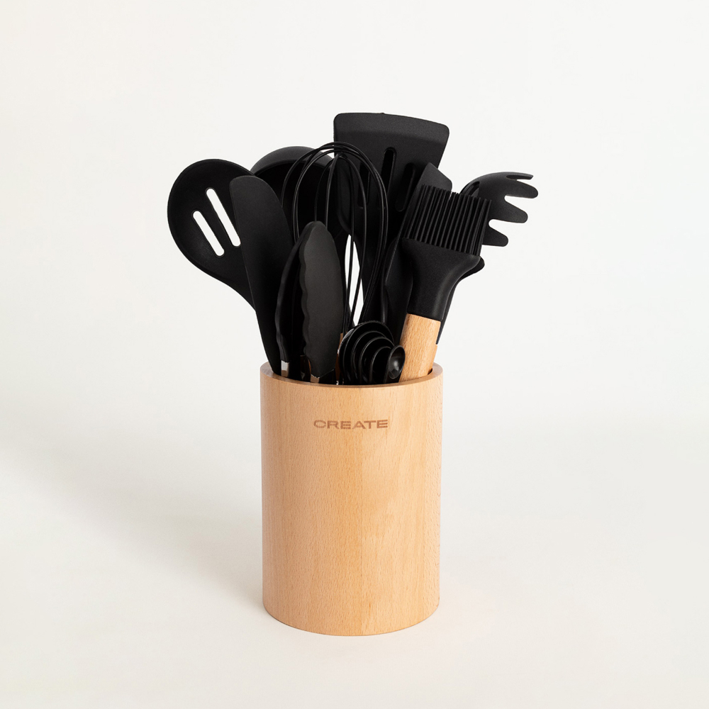 Un juego de utensilios de cocina negros con mangos de madera está ordenado en un soporte cilíndrico de madera.