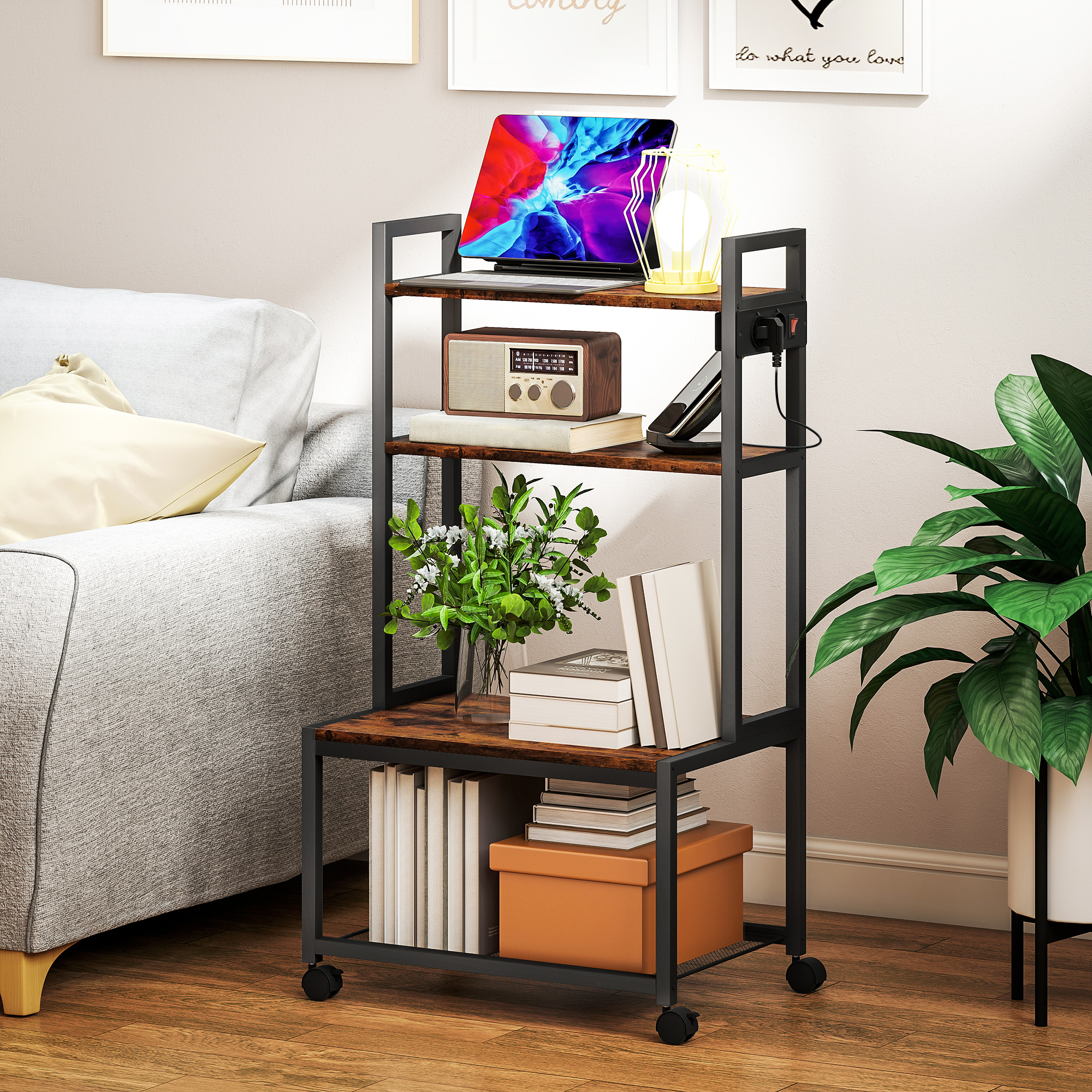 Una mesa auxiliar con ruedas y marco de metal sostiene una computadora portátil, radio, libros y plantas junto a un sofá.