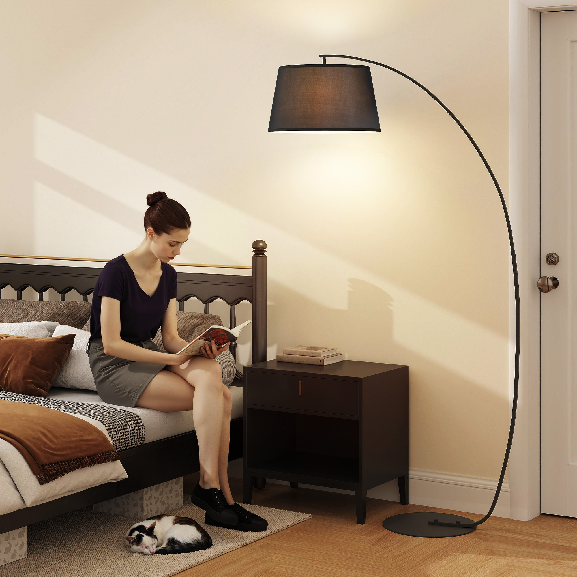 Una mujer lee en la cama junto a una mesita de noche, lámpara de pie arqueada y un gato durmiendo.