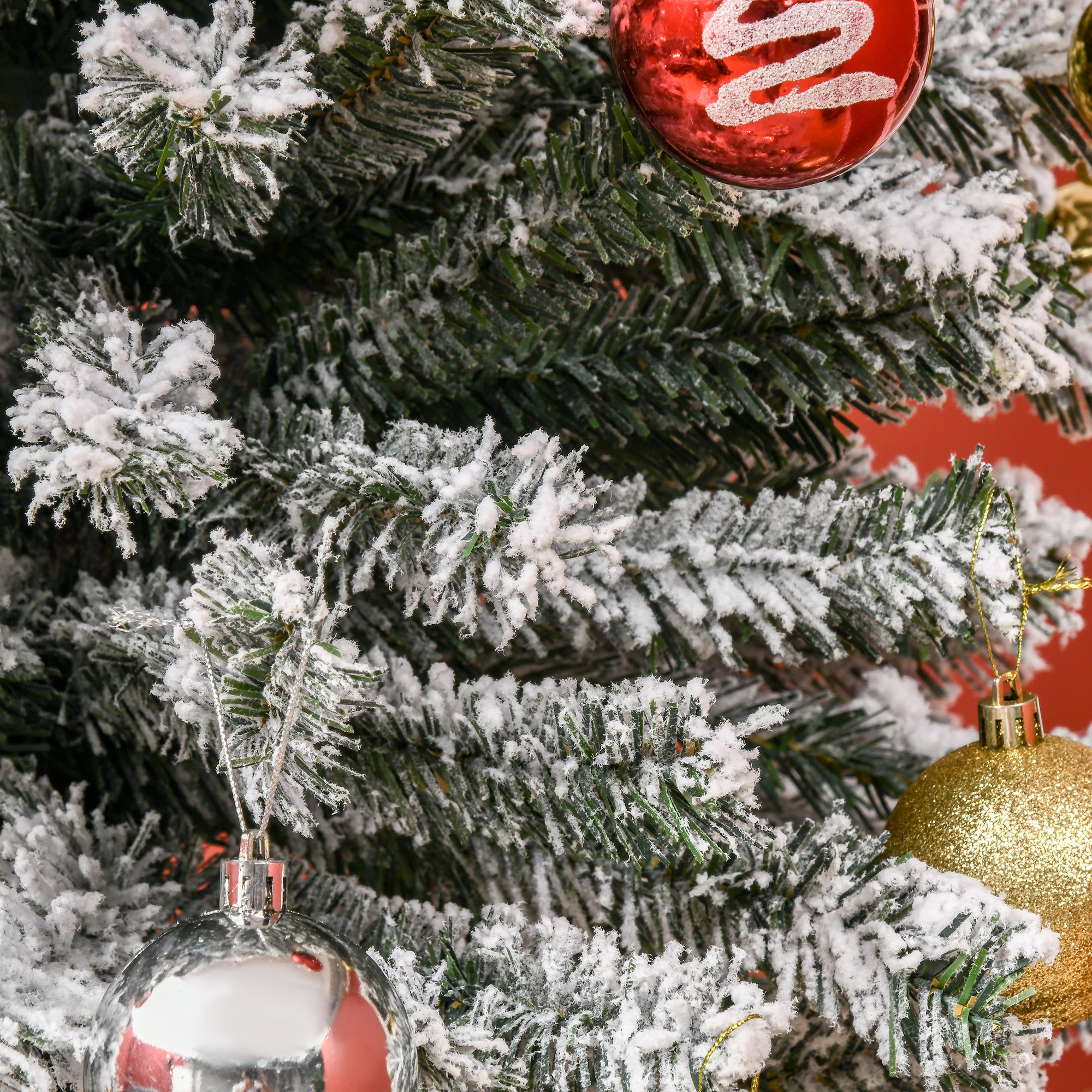 Árbol de navidad cubierto de nieve decorado con bolas rojas, plateadas y doradas.