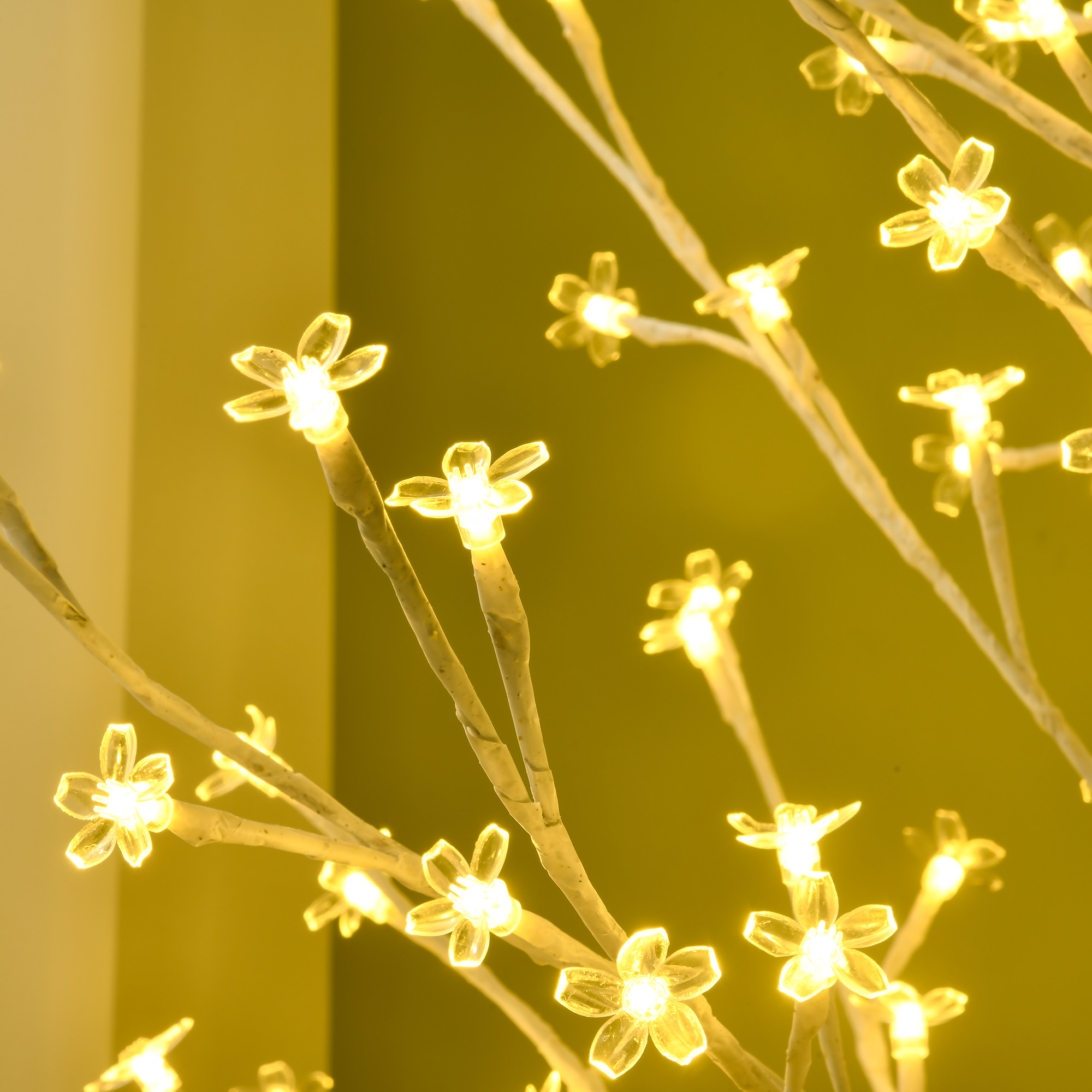 Un árbol artificial blanco con luces de flores amarillas brillantes contra una pared amarilla.
