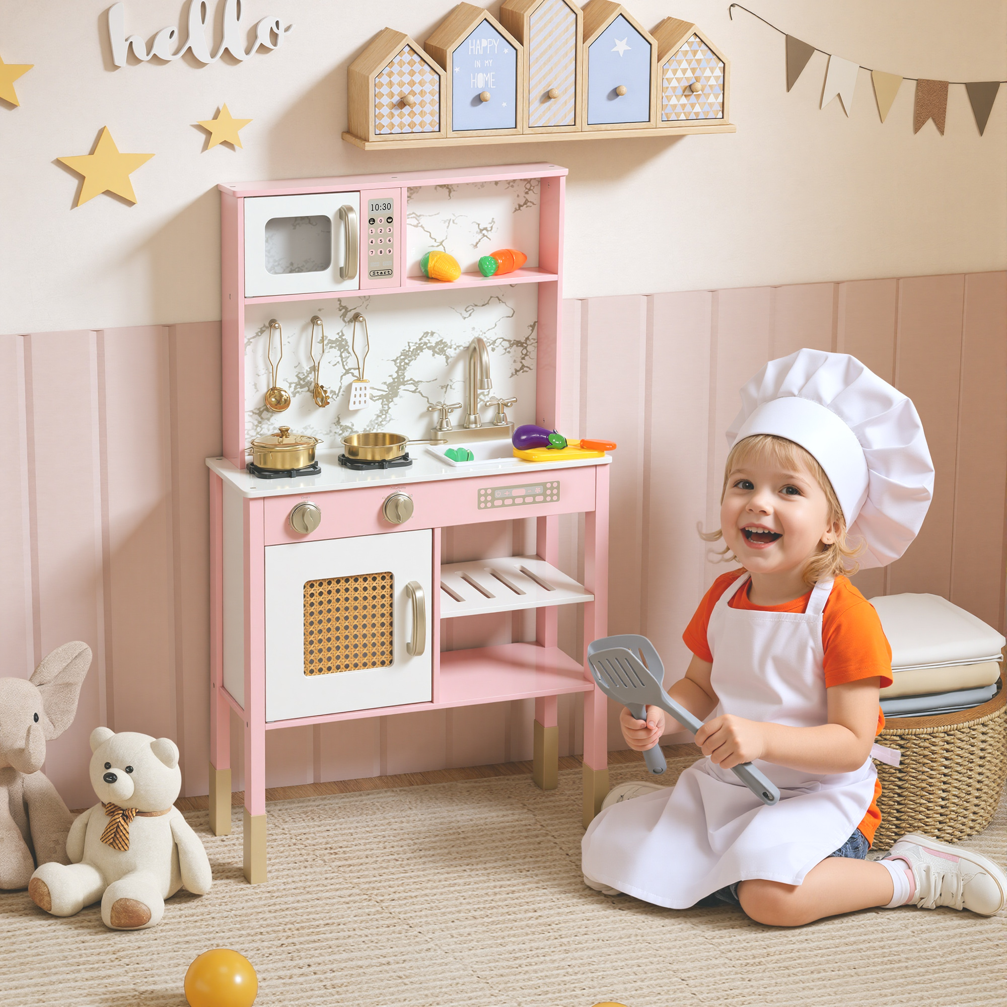 Un niño pequeño con gorro de cocinero y delantal sostiene una espátula de juguete junto a una cocinita rosa.