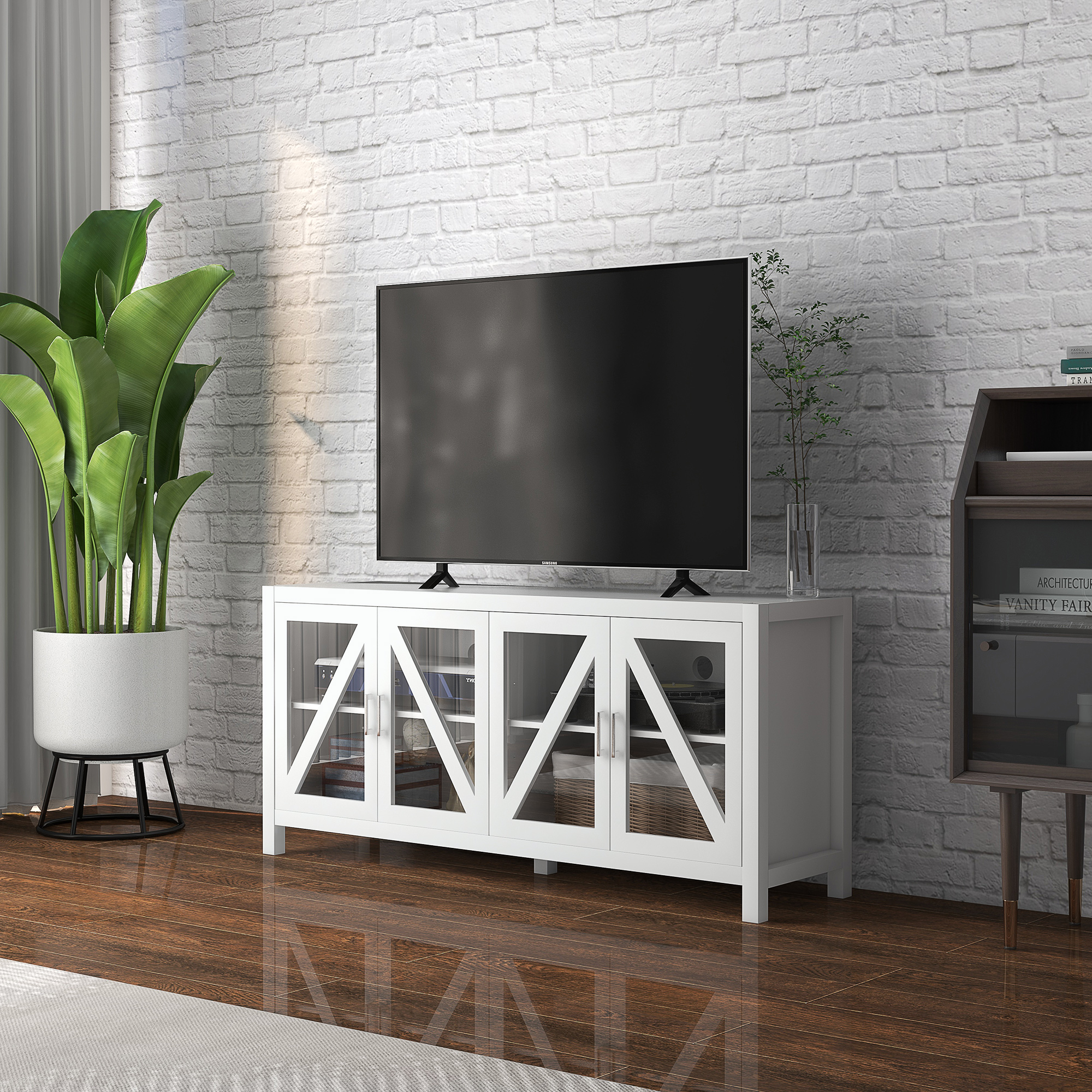 Un televisor en una mesa consola blanca contra una pared de ladrillo blanco, con una planta y un gabinete oscuro.