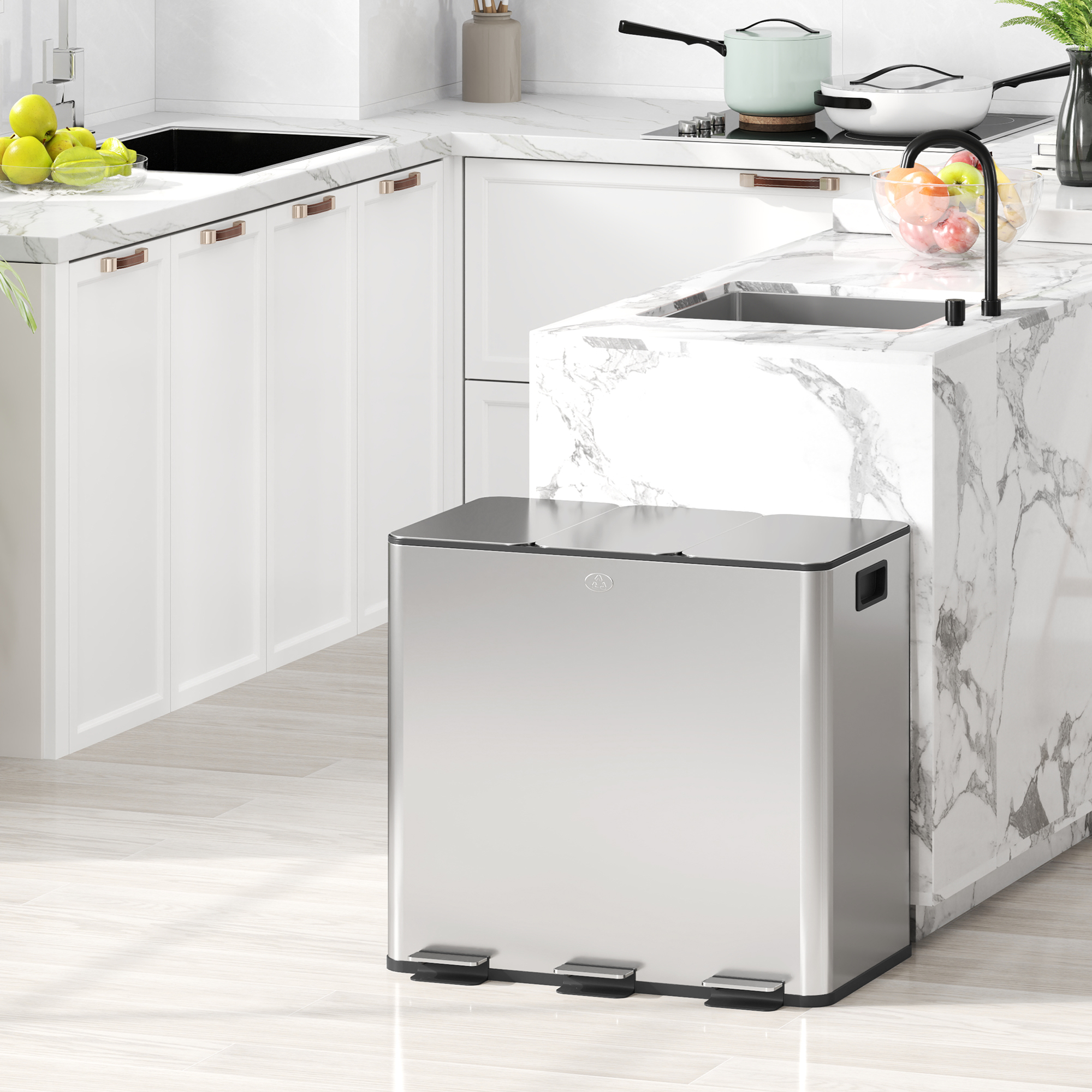 Un cubo de basura plateado con tres pedales se encuentra en una cocina blanca moderna con encimeras de ma