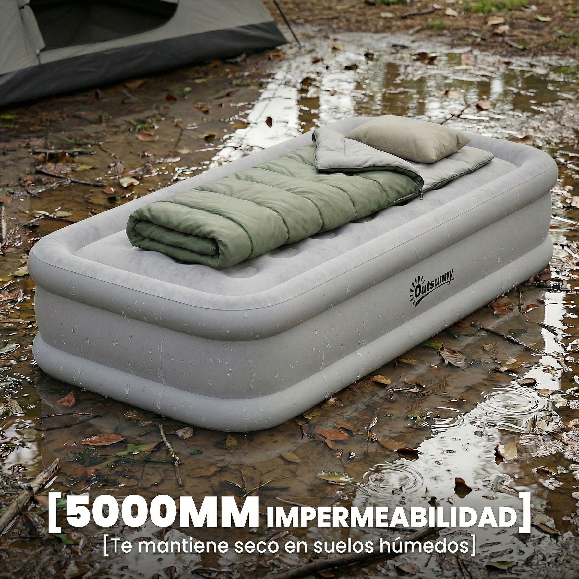 Un colchón inflable gris con saco de dormir verde y almohada sobre suelo húmedo y embarrado.