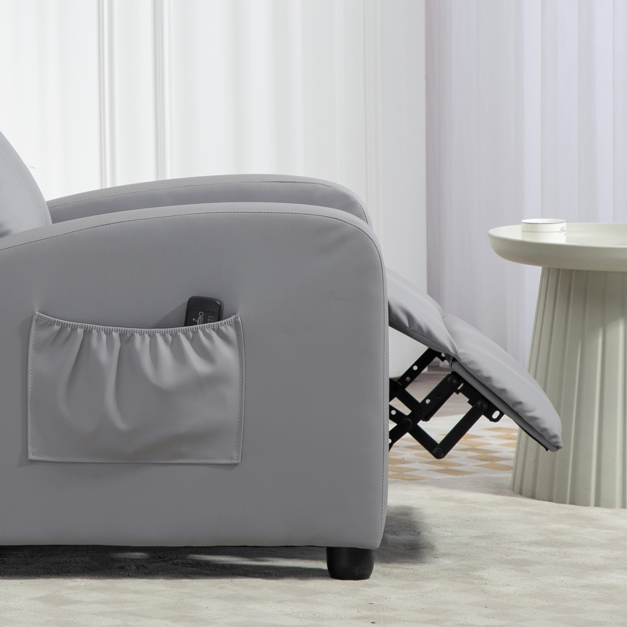 Un sillón gris con reposapiés y bolsillo lateral en una habitación luminosa.