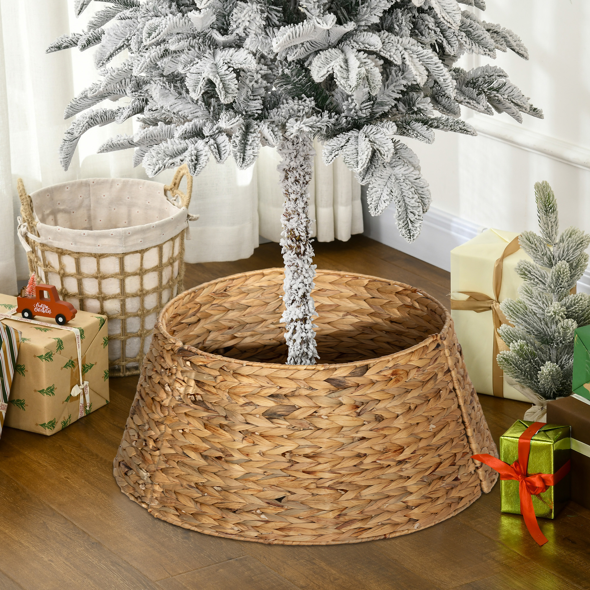 Un árbol de Navidad nevado en un collar de mimbre con regalos, un camión de juguete y una cesta.