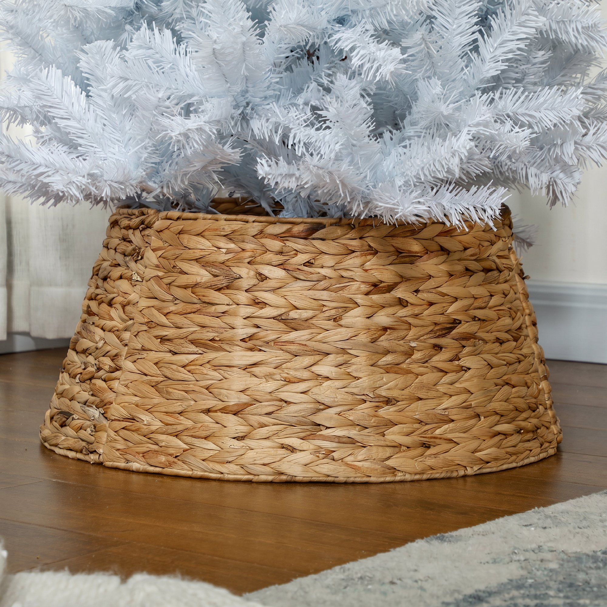 Un árbol de Navidad blanco en una cesta marrón tejida sobre suelo de madera.
