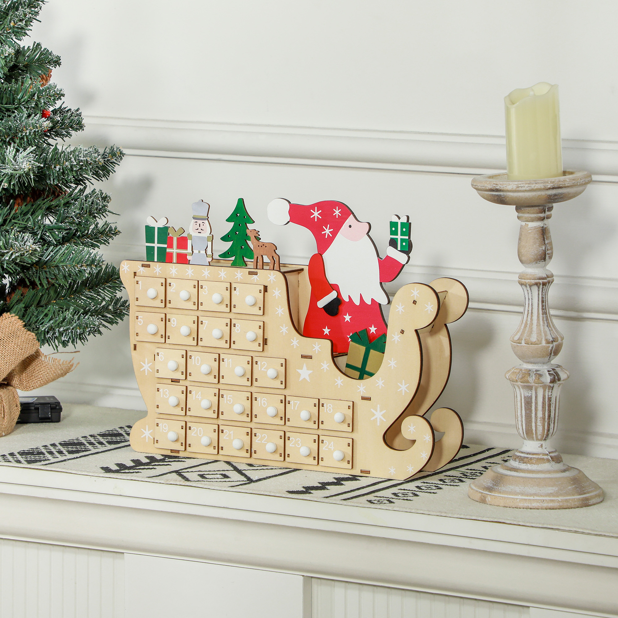 Un calendario de adviento de madera con forma de trineo con Papá Noel, pequeños regalos y un árbol, junto a una vela.