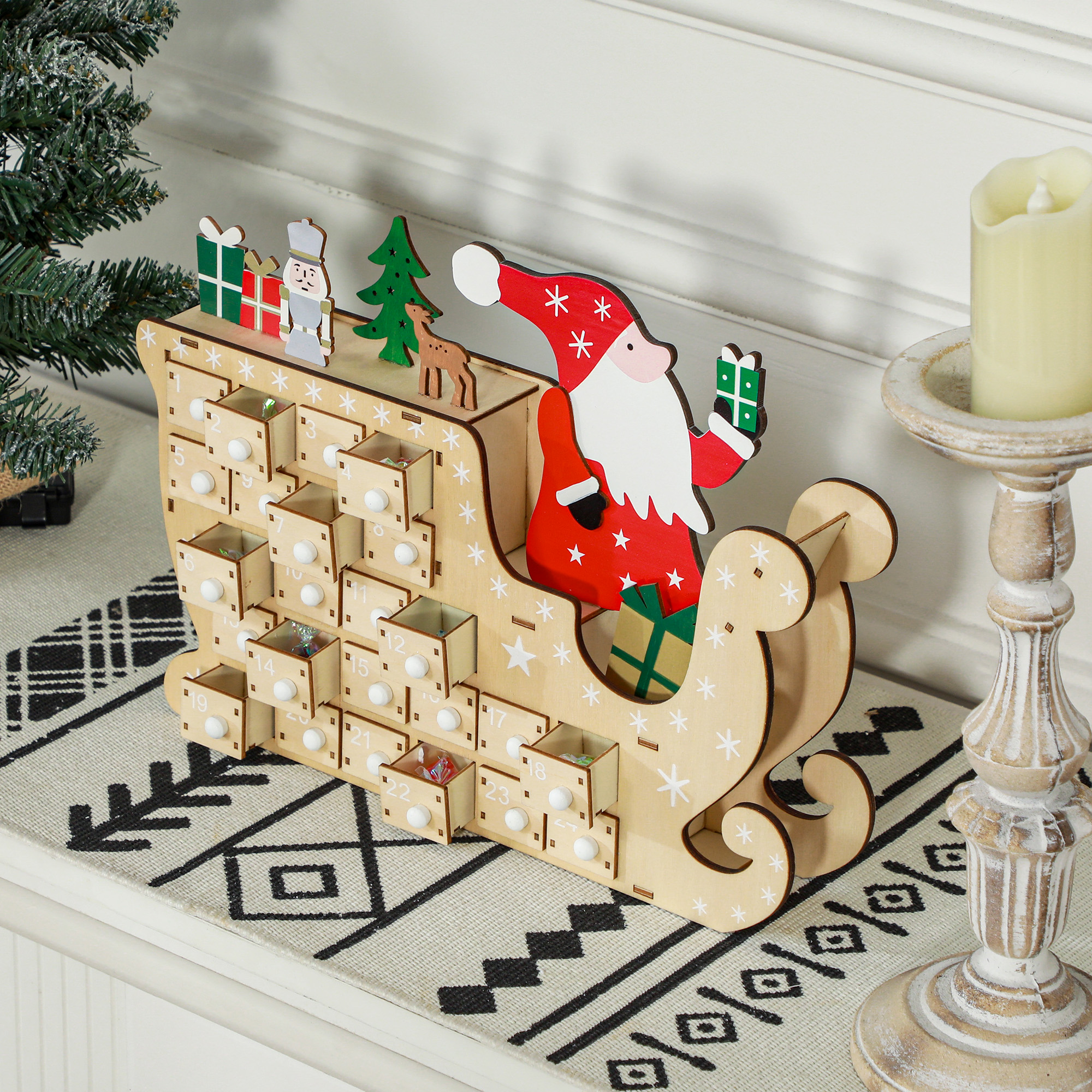 Un calendario de adviento de trineo de Papá Noel de madera con cajones numerados junto a una vela y un árbol.
