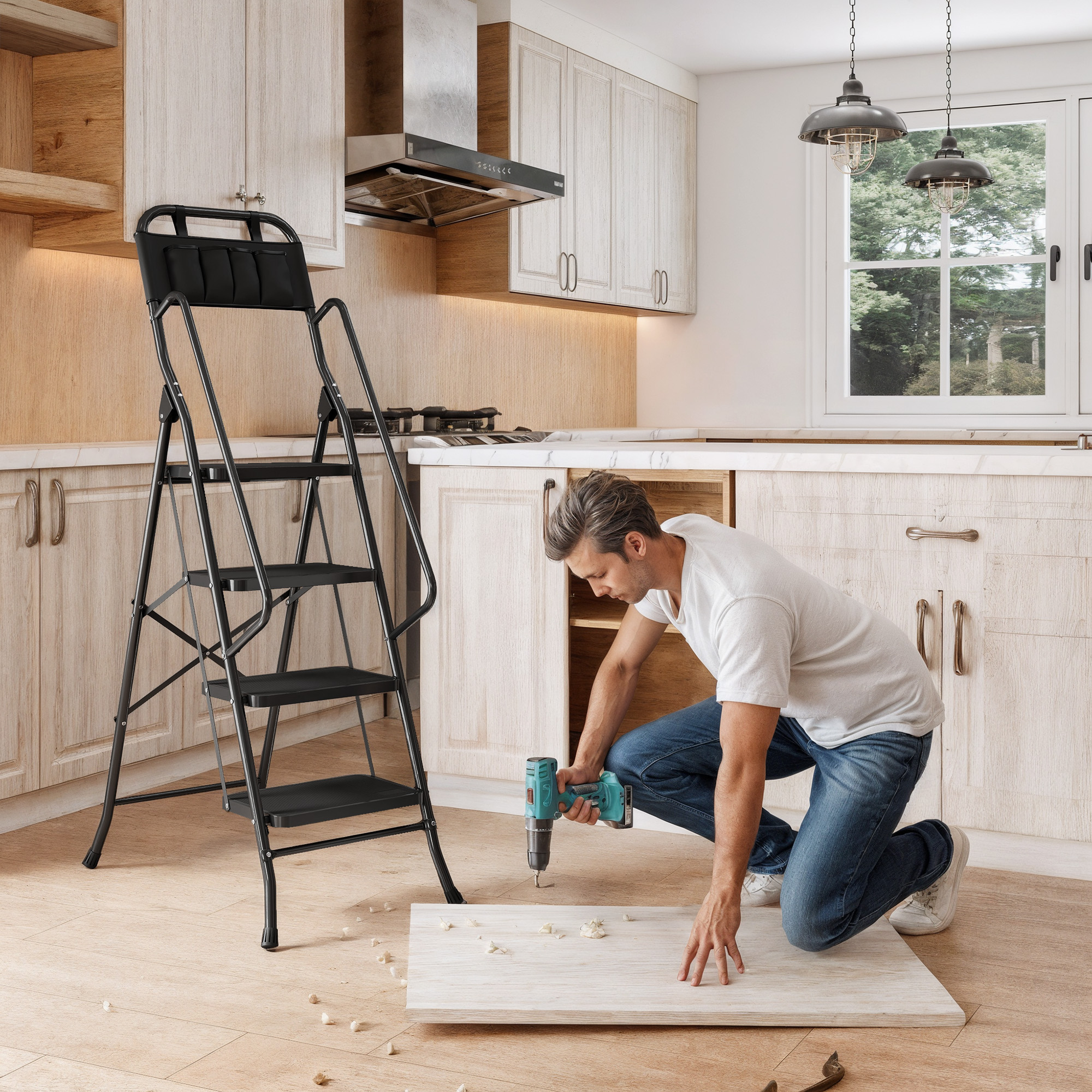 Un hombre se arrodilla en una cocina usando un taladro en una tabla de madera junto a una escalera negra.