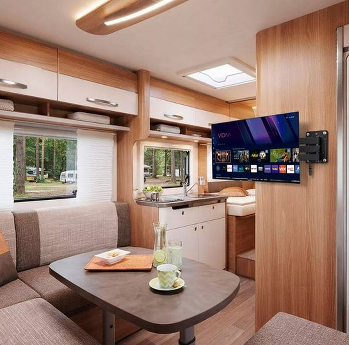 Acogedor interior de autocaravana con mesa, sofá, cocina americana y televisor de pared.