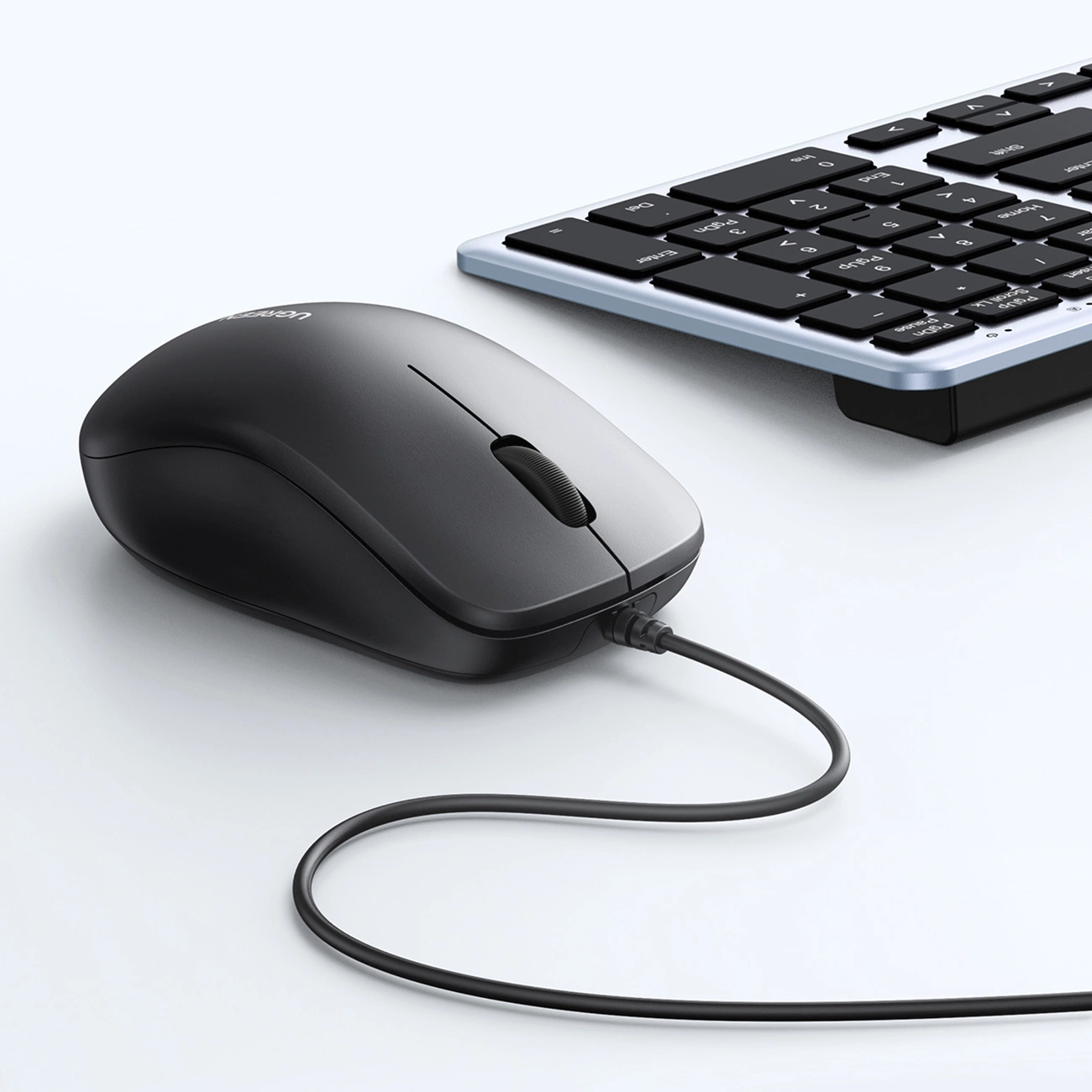 Un ratón de ordenador negro con cable y un teclado colocados sobre una superficie clara.