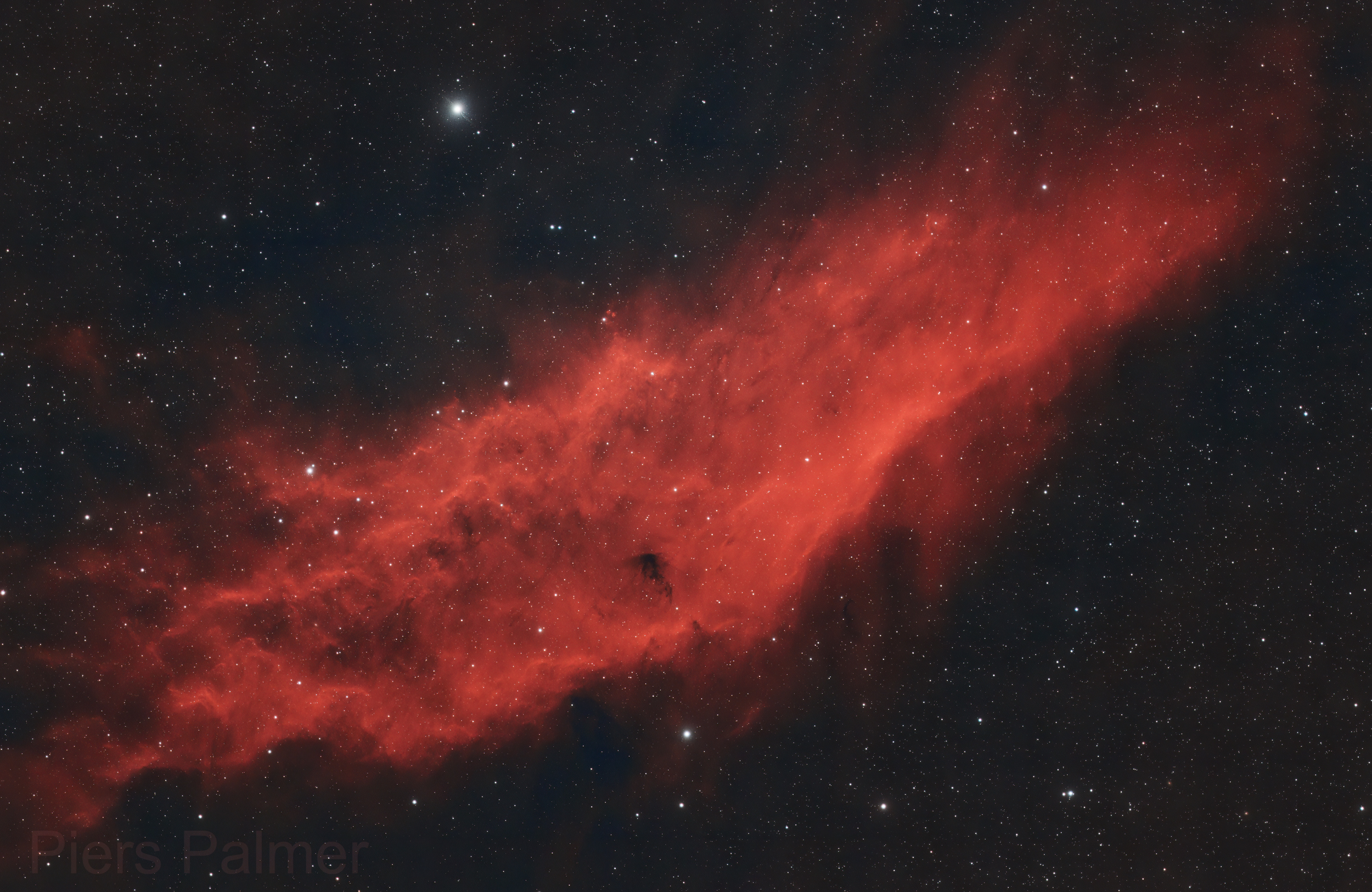 Una vibrante Nebulosa California roja brilla contra un cielo nocturno estrellado con detalles estelares.