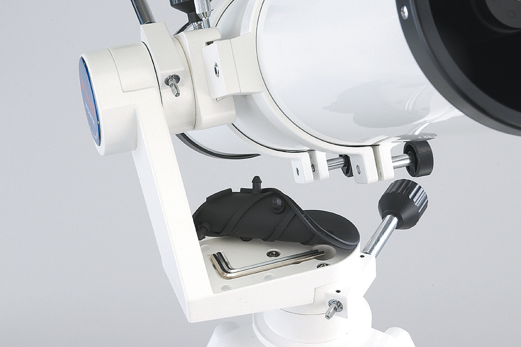 Primer plano de un telescopio blanco que muestra su montura, perillas de ajuste y herramientas.