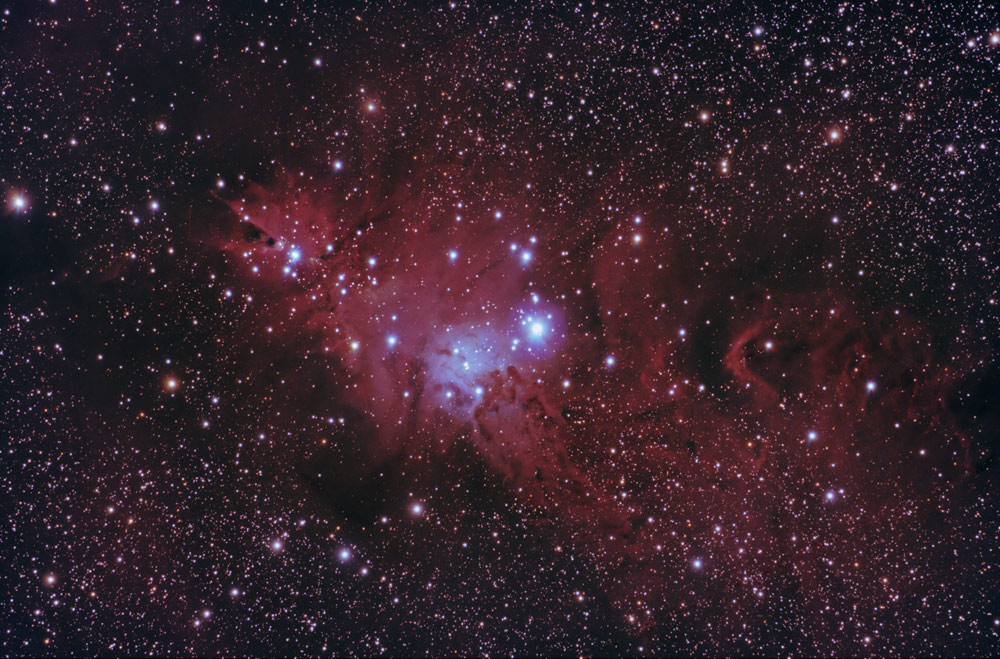 Un vasto campo de innumerables estrellas brillantes y nubes de gas interestelar rojizas en el universo oscuro.