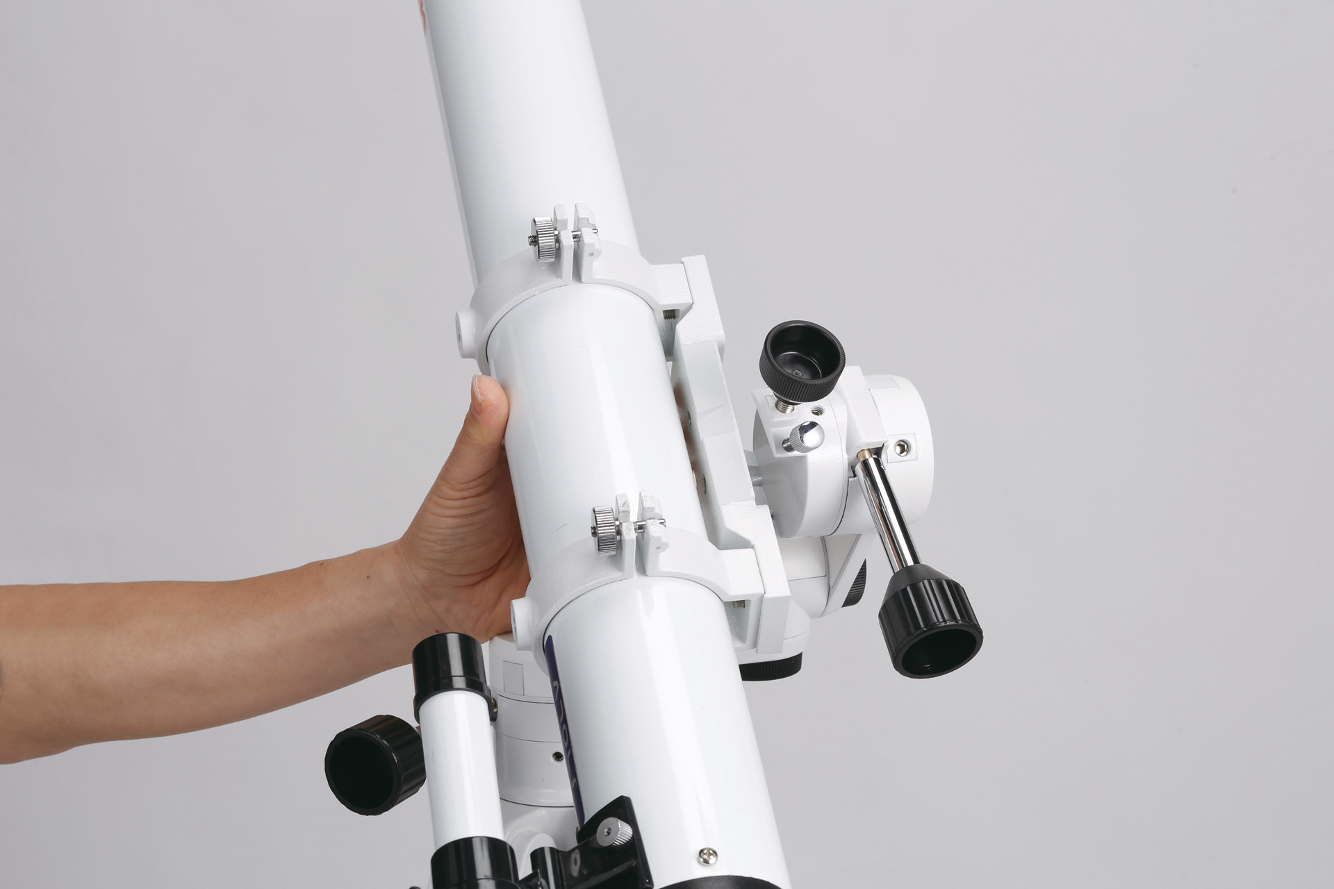Una mano sostiene un tubo de telescopio blanco sobre fondo gris.