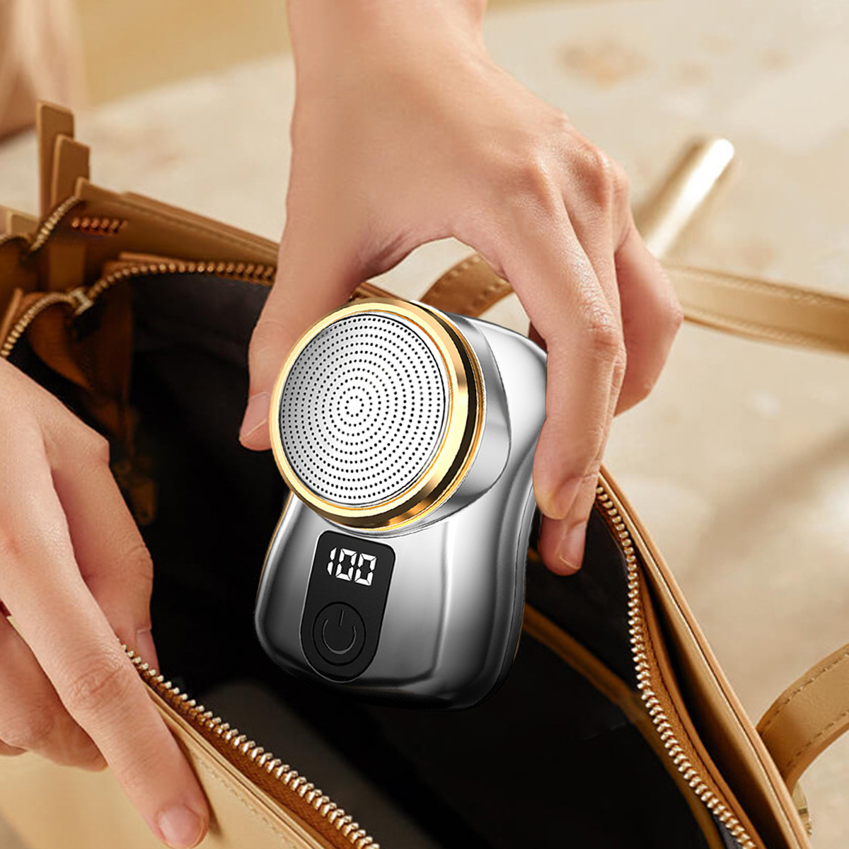 Eine Hand legt einen kleinen silber-goldenen Elektrorasierer in eine offene braune Handtasche.