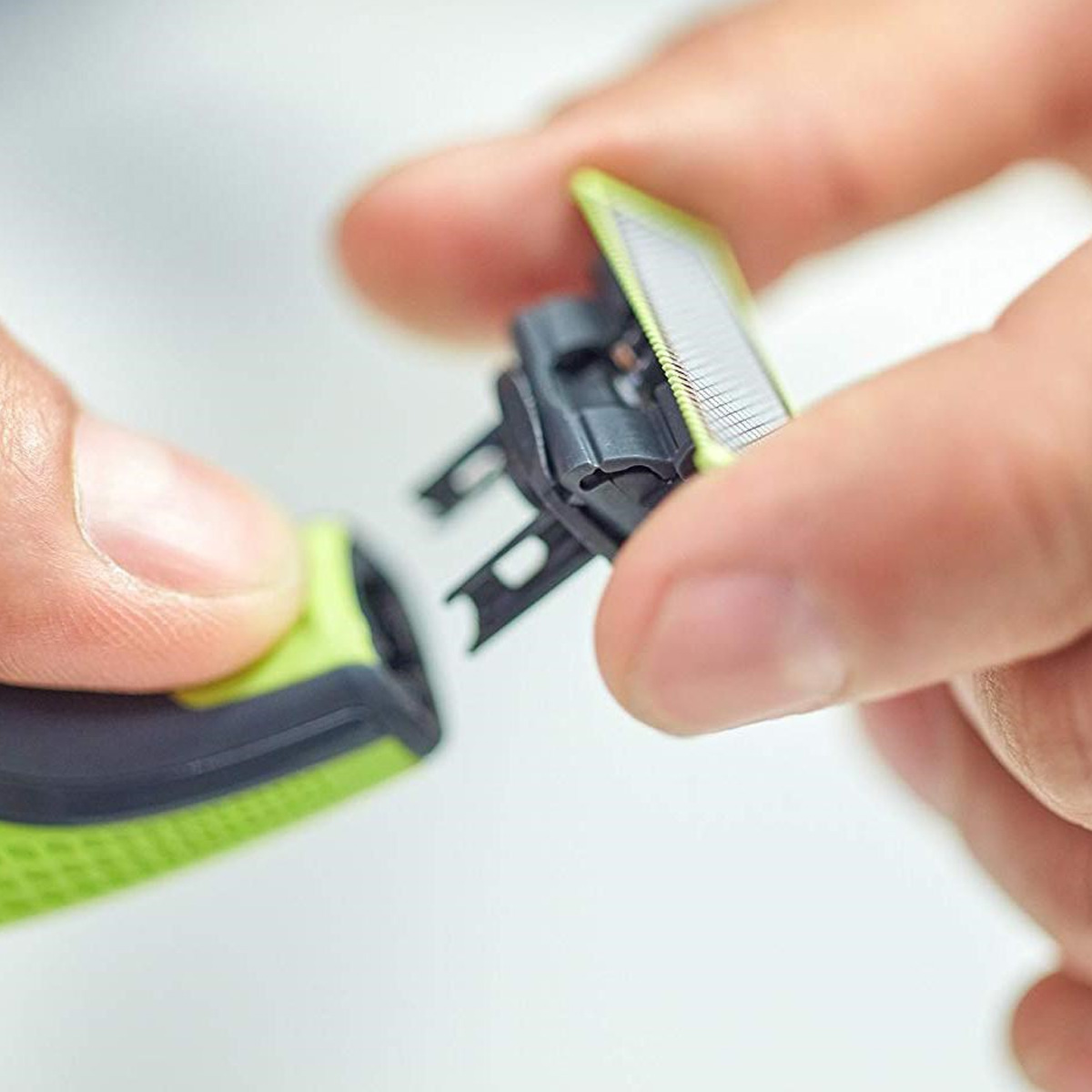 Hände wechseln den Scherkopf eines elektrischen Rasierers aus.