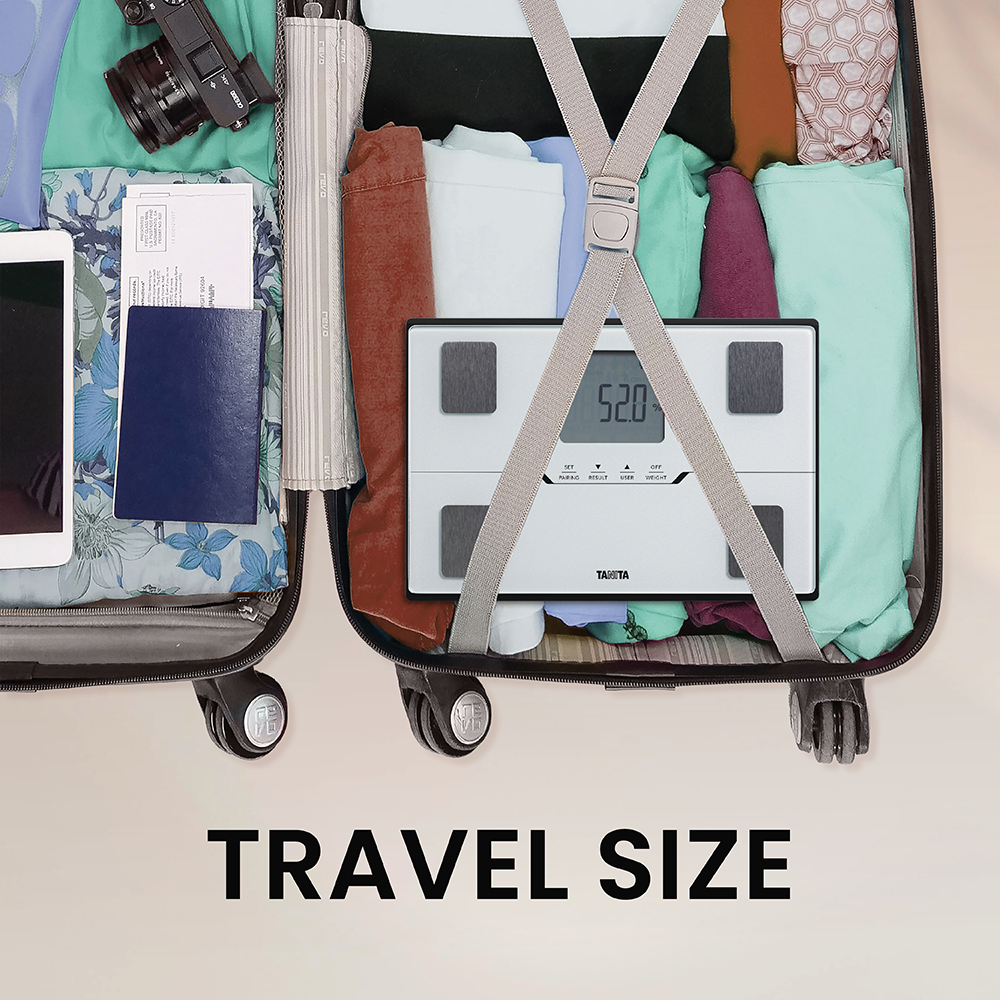 Une valise ouverte remplie de vêtements, appareil photo, passeport, tablette et une balance Tanita.