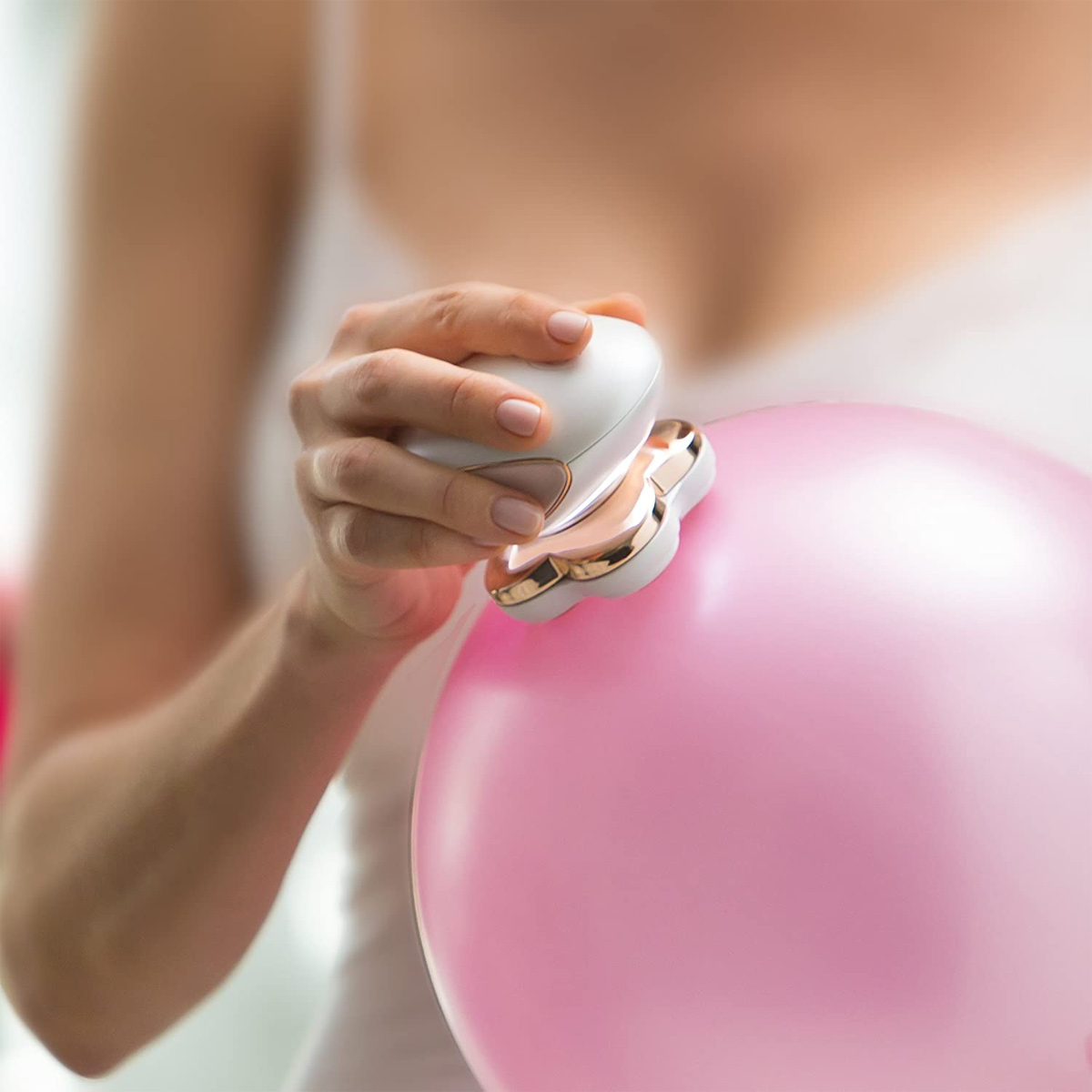 Eine Hand hält ein weißes und roségoldenes Enthaarungsgerät an einen rosa Ballon.