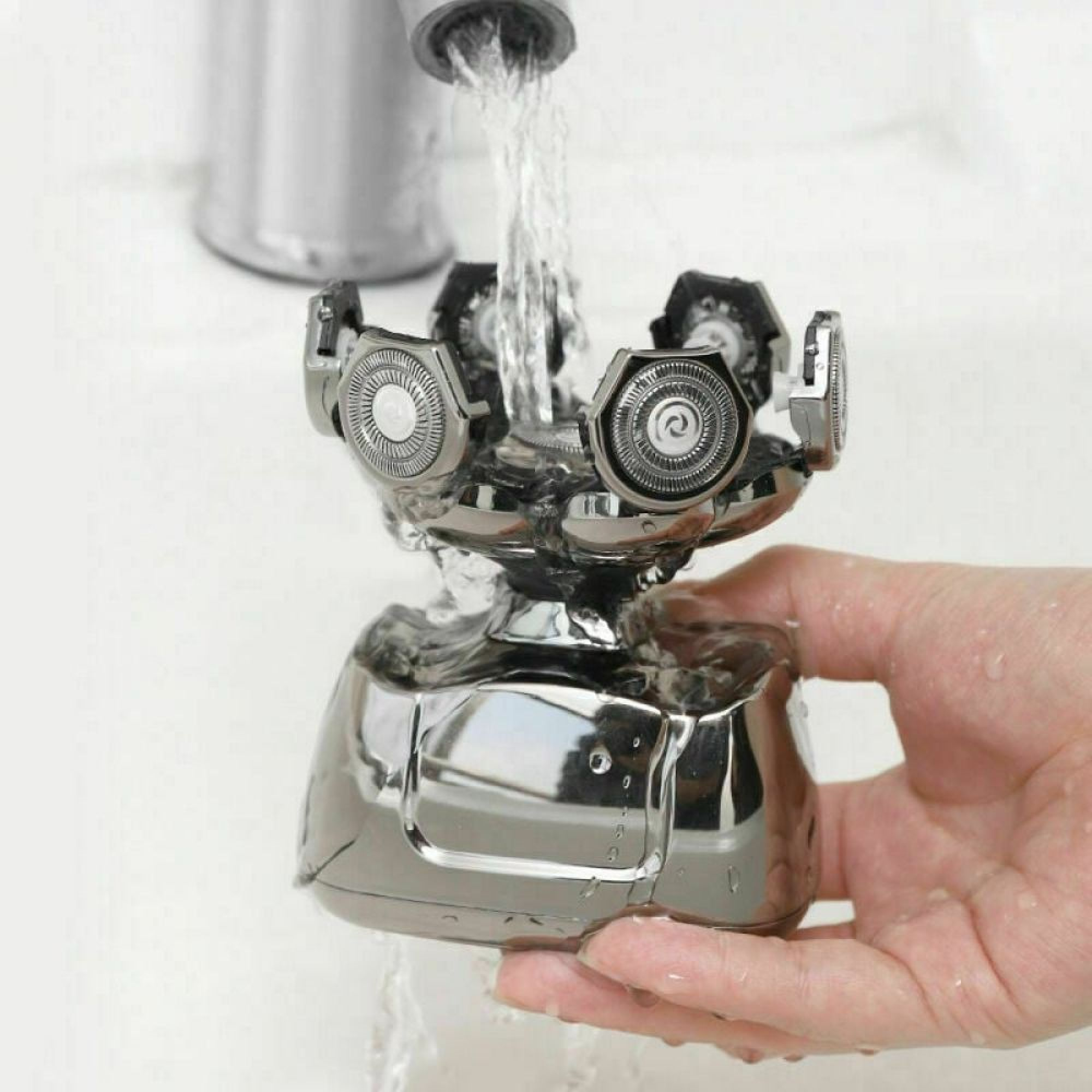 Wasser fließt aus einem Hahn über den Kopf eines elektrischen Rasierers in einer Hand.